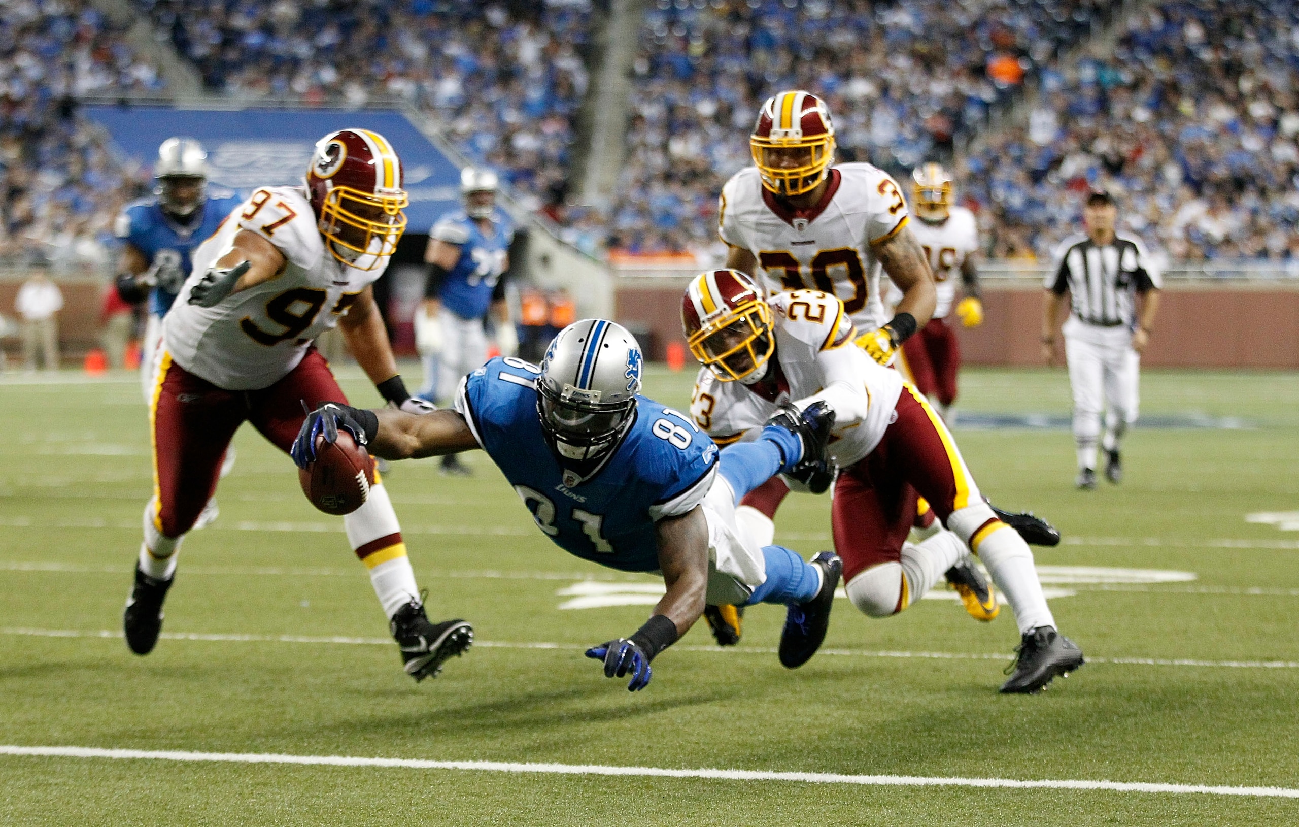 DETROIT - OCTOBER 31: Calvin Johnson #81 of the Detroit Lions scores a second quarter touchdown as DeAngelo Hall #23 and Lorenzo Alexander #97 of the Washington Redskins attempt tp make the stop at Ford Field on October 31, 2010 in Detroit, Michigan. (Pho DETROIT - OCTOBER 31: Calvin Johnson #81 of the Detroit Lions scores a second quarter touchdown as DeAngelo Hall #23 and Lorenzo Alexander #97 of the Washington Redskins attempt tp make the stop at Ford Field on October 31, 2010 in Detroit, Michigan. (Pho