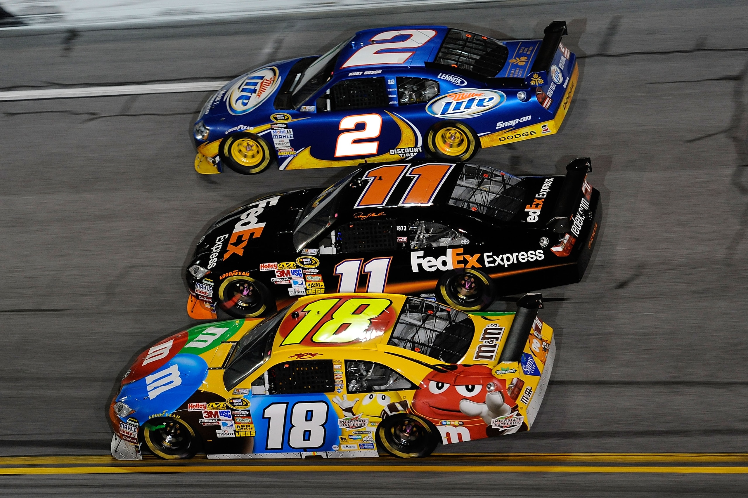 DAYTONA BEACH, FL - FEBRUARY 06:  Kyle Busch, driver of the #18 M&M's Toyota, races Denny Hamlin, driver of the #11 FedEx Toyota, and Kurt Busch, driver of the #2 Miller Lite Dodge, during the Budweiser Shootout at Daytona International Speedway on Februa