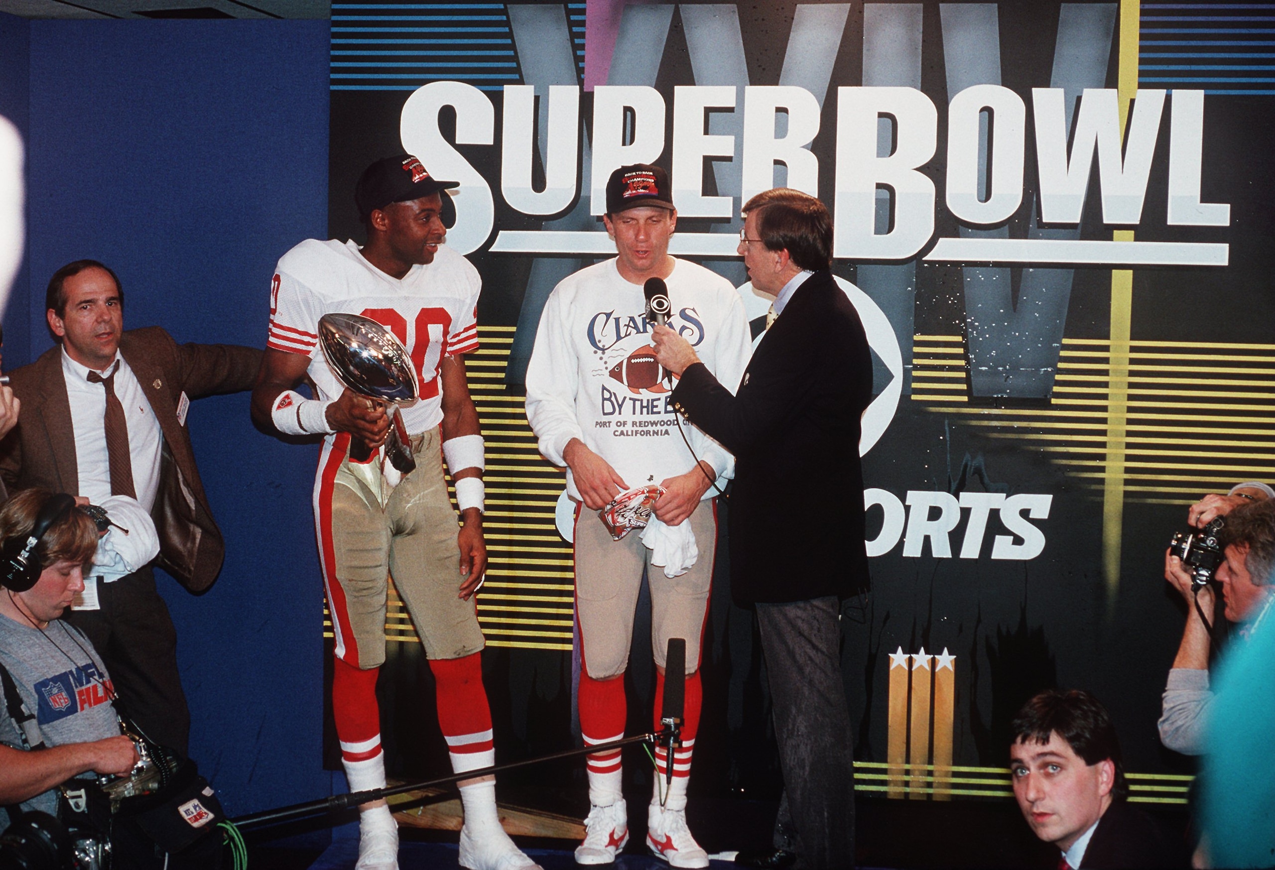 28 Jan 1990: SAN FRANCISCO QUARTERBACK JOE MONTANA TALKS WITH BRENT MUSBURGER OF CBS SPORTS, AS WIDE RECEIVER JERRY RICE HOLDS THE SUPER BOWL TROPHY, FOLLOWING THE 49ERS 55-10 VICTORY OVER THE DENVER BRONCOS IN SUPER BOWL XXIV AT THE SUPERDOME IN NEW ORLE
