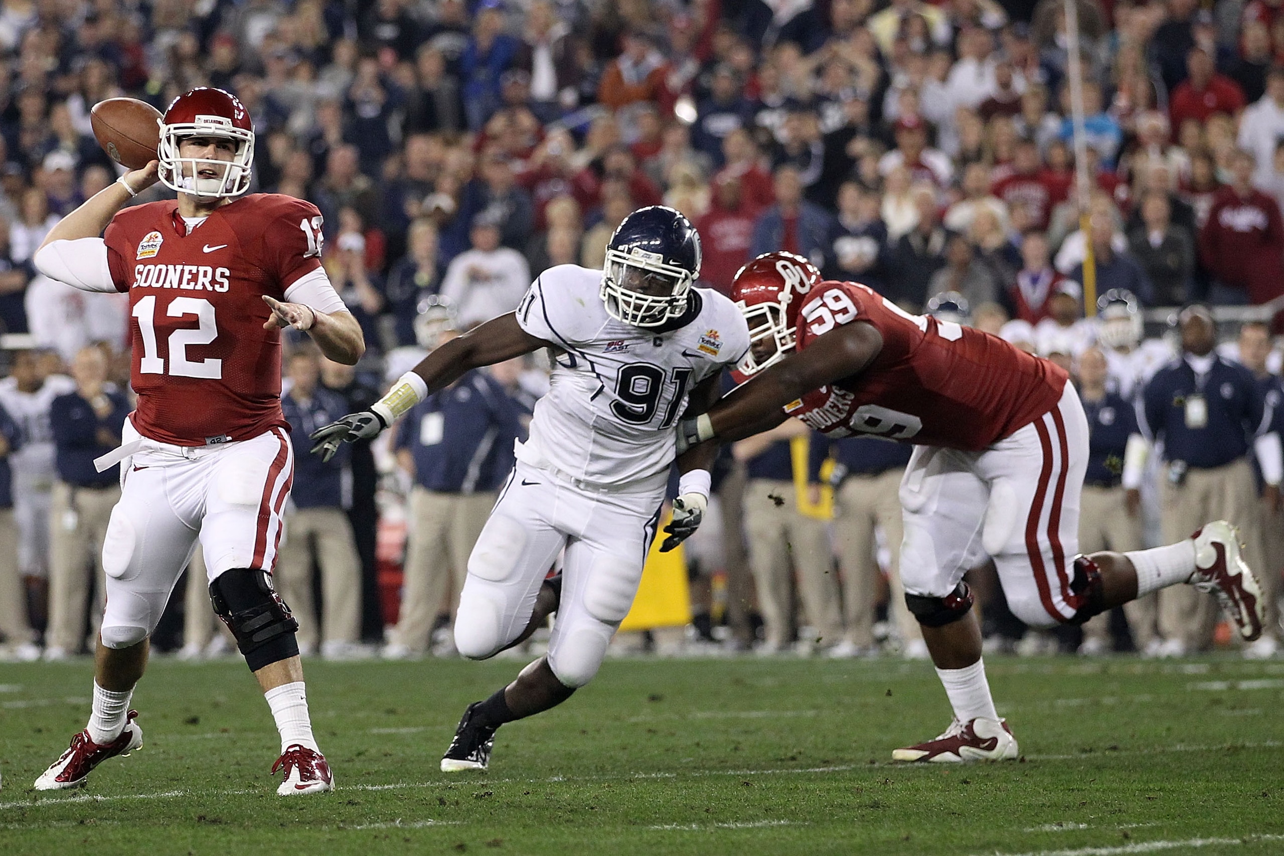 GLENDALE, AZ - JANUARY 01: Landry Jones #12 of the Oklahoma Sooners passes the ball as Jesse Joseph #91 of the Connecticut Huskies rushes in past Donald Stephenson #59 of the Sooners in the first half against the Connecticut Huskies during the Tostitos F GLENDALE, AZ - JANUARY 01: Landry Jones #12 of the Oklahoma Sooners passes the ball as Jesse Joseph #91 of the Connecticut Huskies rushes in past Donald Stephenson #59 of the Sooners in the first half against the Connecticut Huskies during the Tostitos F