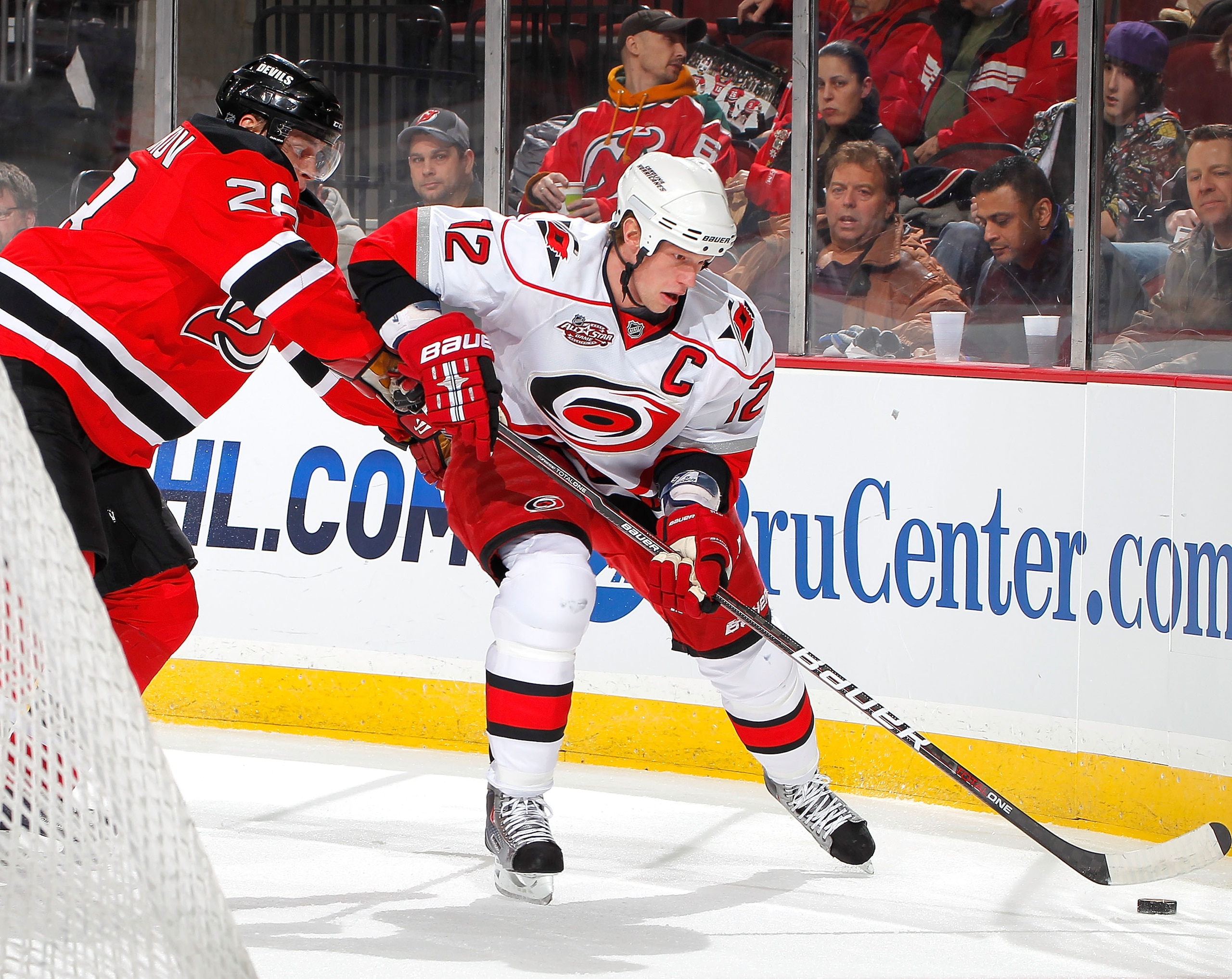 NEWARK, NJ - FEBRUARY 08:  Eric Staal #12 of the Carolina Hurricanes is checked Anton Volchenkov #28 of the New Jersey Devils during the first period of an NHL hockey game at the Prudential Center on February 8, 2011 in Newark, New Jersey.  (Photo by Paul