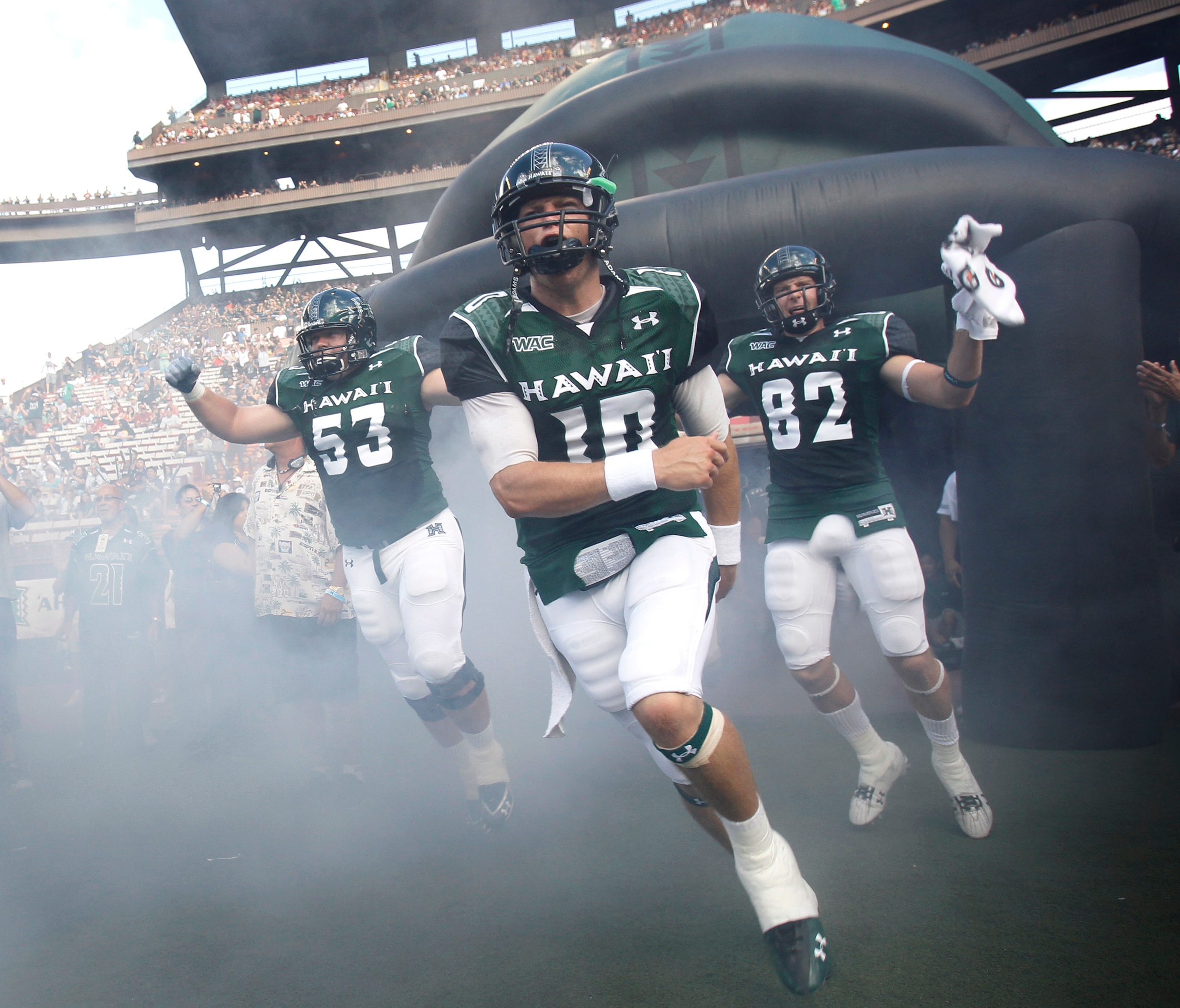 HONOLULU - SEPTEMBER 02: Levi Legay #53, Shane Austin #10, and Jett Jasper #82 of the University of Hawaii Warriors and other team members rush out of the tunnel to take the field in their season opener against the University of Southern California Trojan