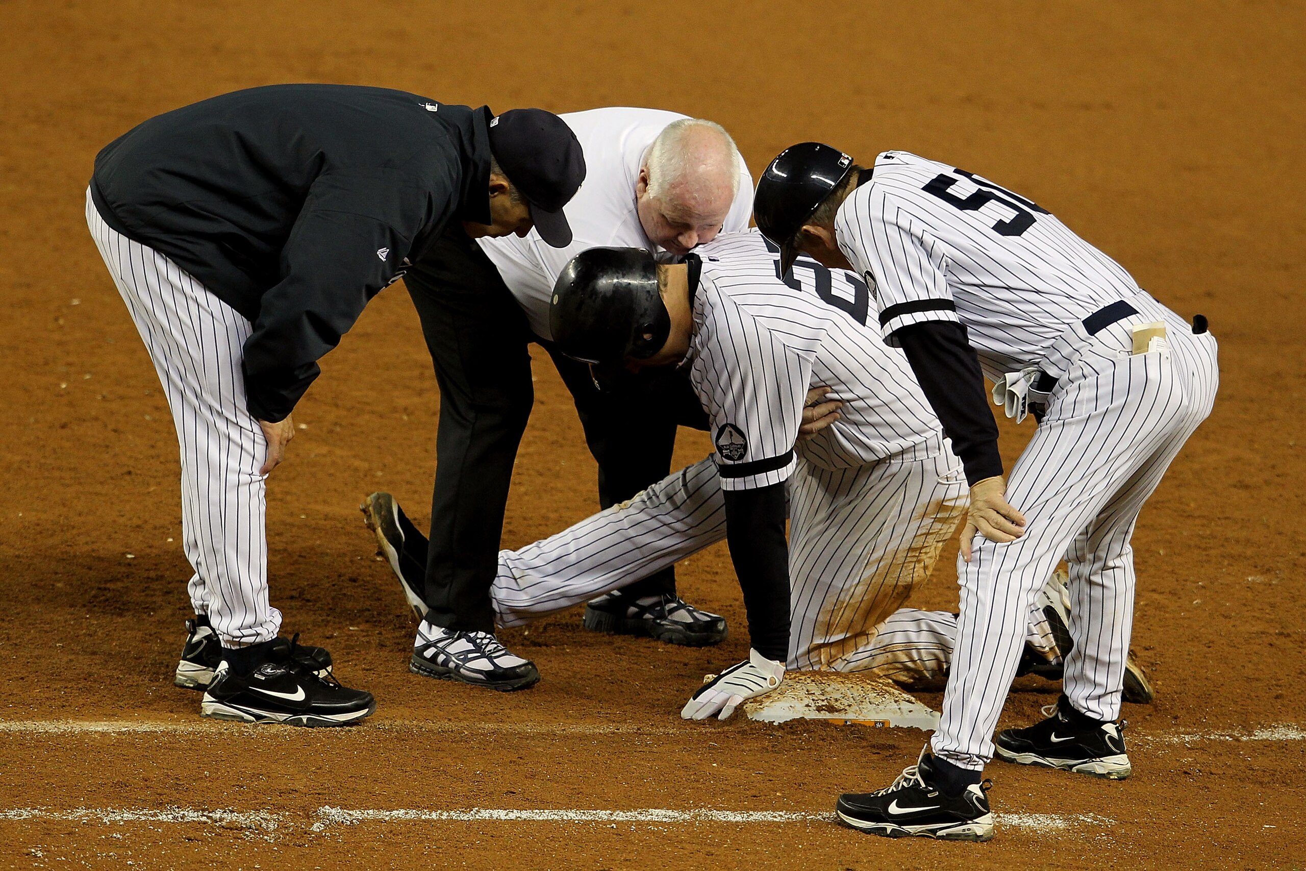 NEW YORK - OCTOBER 19:  Mark Teixeira #25 of the New York Yankees is tended to by Manager Joe Girardi after hurting himself as first base coach Mick Kelleher #50 looks on while playing against the Texas Rangers in Game Four of the ALCS during the 2010 MLB