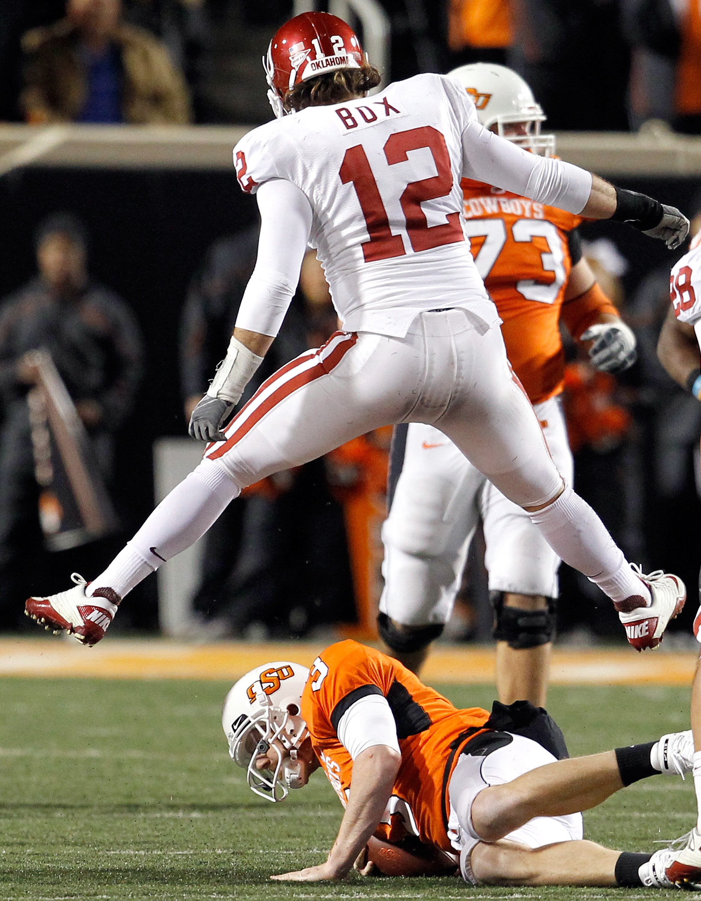 STILLWATER, OK - NOVEMBER 27:  Linebacker Austin Box #12 of the Oklahoma Sooners leaps over quarterback Brandon Weeden #3 of the Oklahoma State Cowboys after Weeden was sacked for a loss at Boone Pickens Stadium on November 27, 2010 in Stillwater, Oklahom