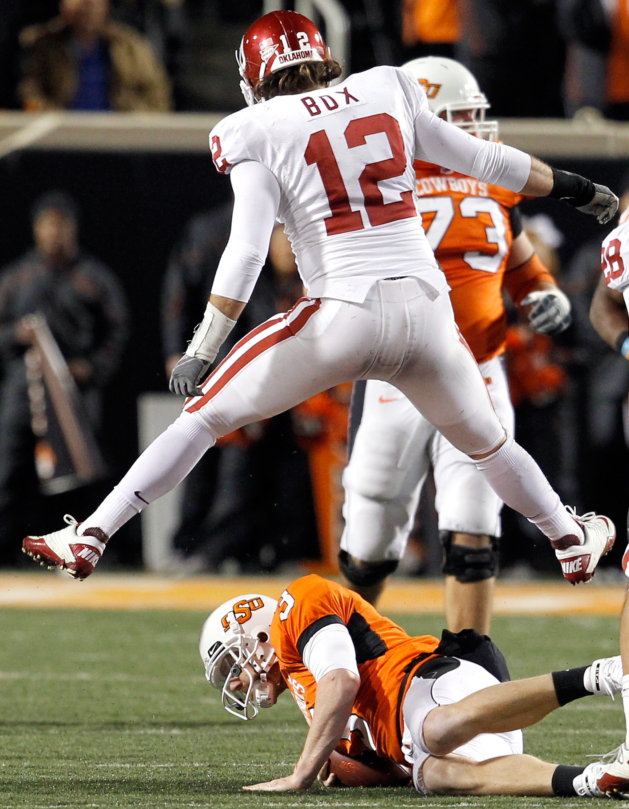 STILLWATER, OK - NOVEMBER 27:  Linebacker Austin Box #12 of the Oklahoma Sooners leaps over quarterback Brandon Weeden #3 of the Oklahoma State Cowboys after Weeden was sacked for a loss at Boone Pickens Stadium on November 27, 2010 in Stillwater, Oklahom