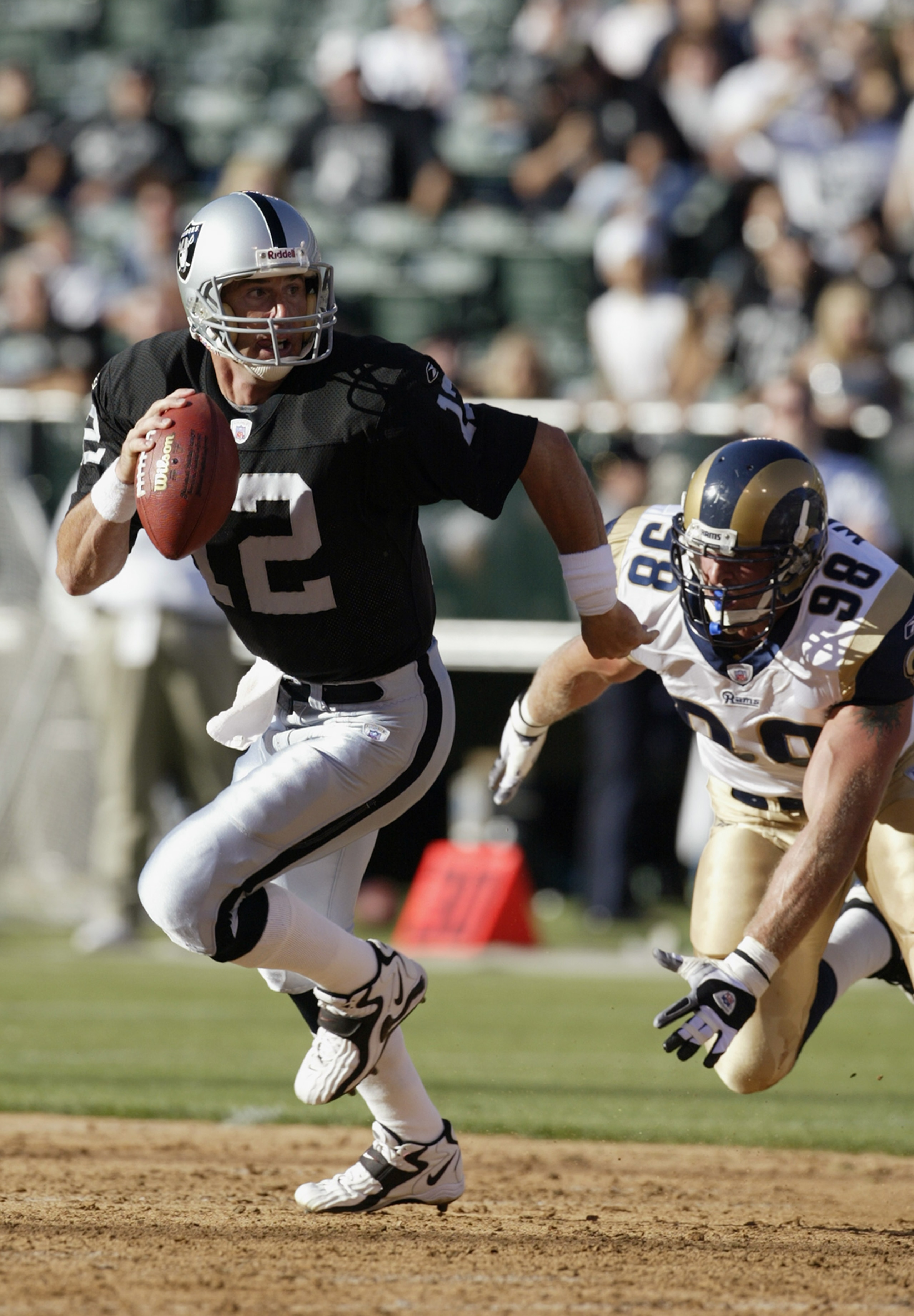OAKLAND, CA - AUGUST 8:  Rich Gannon #12 of the Oakland Raiders looks down the field as he runs away from Grant Wistrom #98 of the St. Louis Rams at the Network Associates Coliseum on August 8, 2003 in Oakland, California.  The Raiders defeated the Rams 7