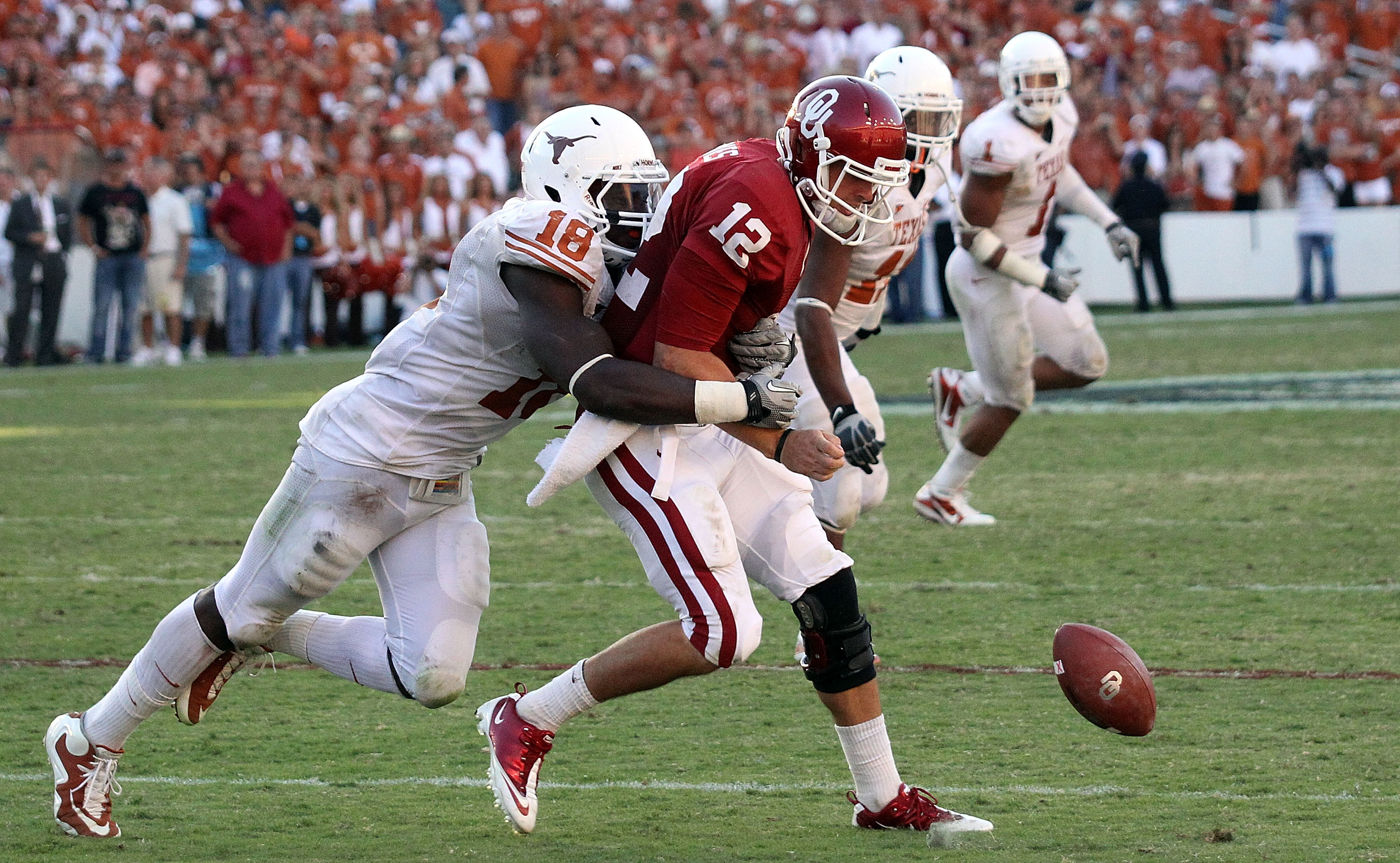 DALLAS - OCTOBER 02:  Quarterback Landry Jones #12 of the Oklahoma Sooners fumbles the ball against D.J. Grant #18 of the Texas Longhorns in the fourth quarter at the Cotton Bowl on October 2, 2010 in Dallas, Texas.  (Photo by Ronald Martinez/Getty Images