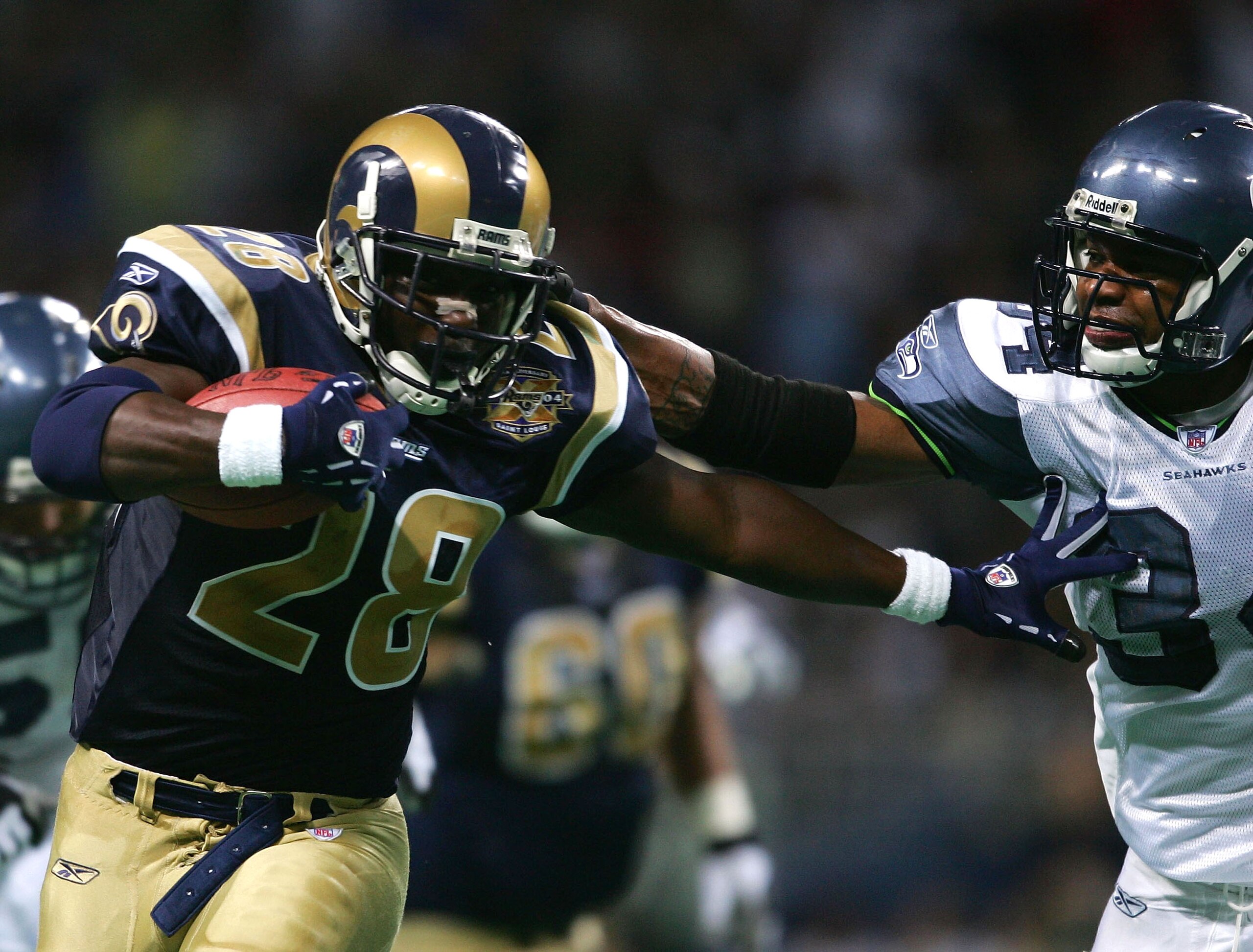 ST. LOUIS - NOVEMBER 14:  Marshall Faulk #28 of the St. Louis Rams carries the ball as Terreal Bierria #34 of the Seattle Seahawks tries make the stop on November 14, 2004 at the Edward Jones Dome in St. Louis, Missouri. The St. Louis Rams defeated the Se