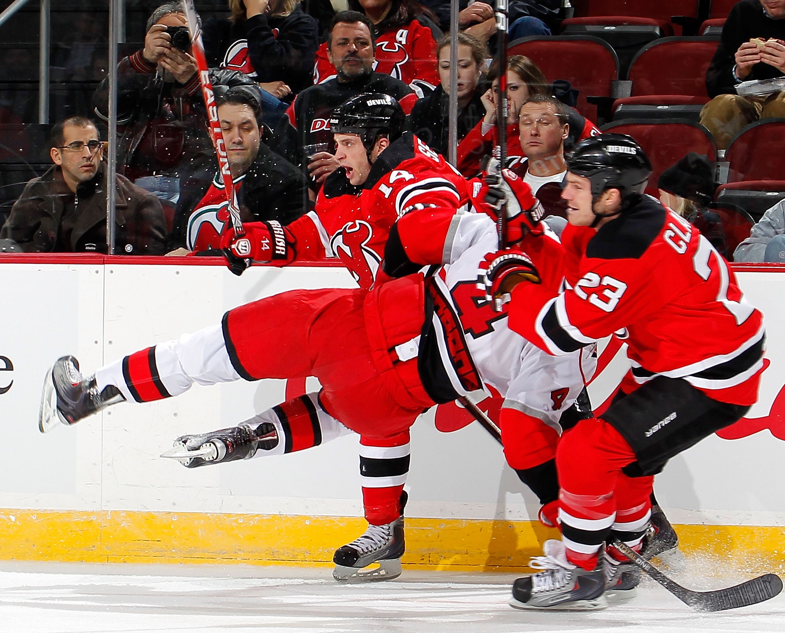NEWARK, NJ - FEBRUARY 08:  Jamie McBain #4 of the Carolina Hurricanes is upended by Tim Sestito #14 and David Clarkson #23 of the New Jersey Devils during the third period of an NHL hockey game at the Prudential Center on February 8, 2011 in Newark, New J