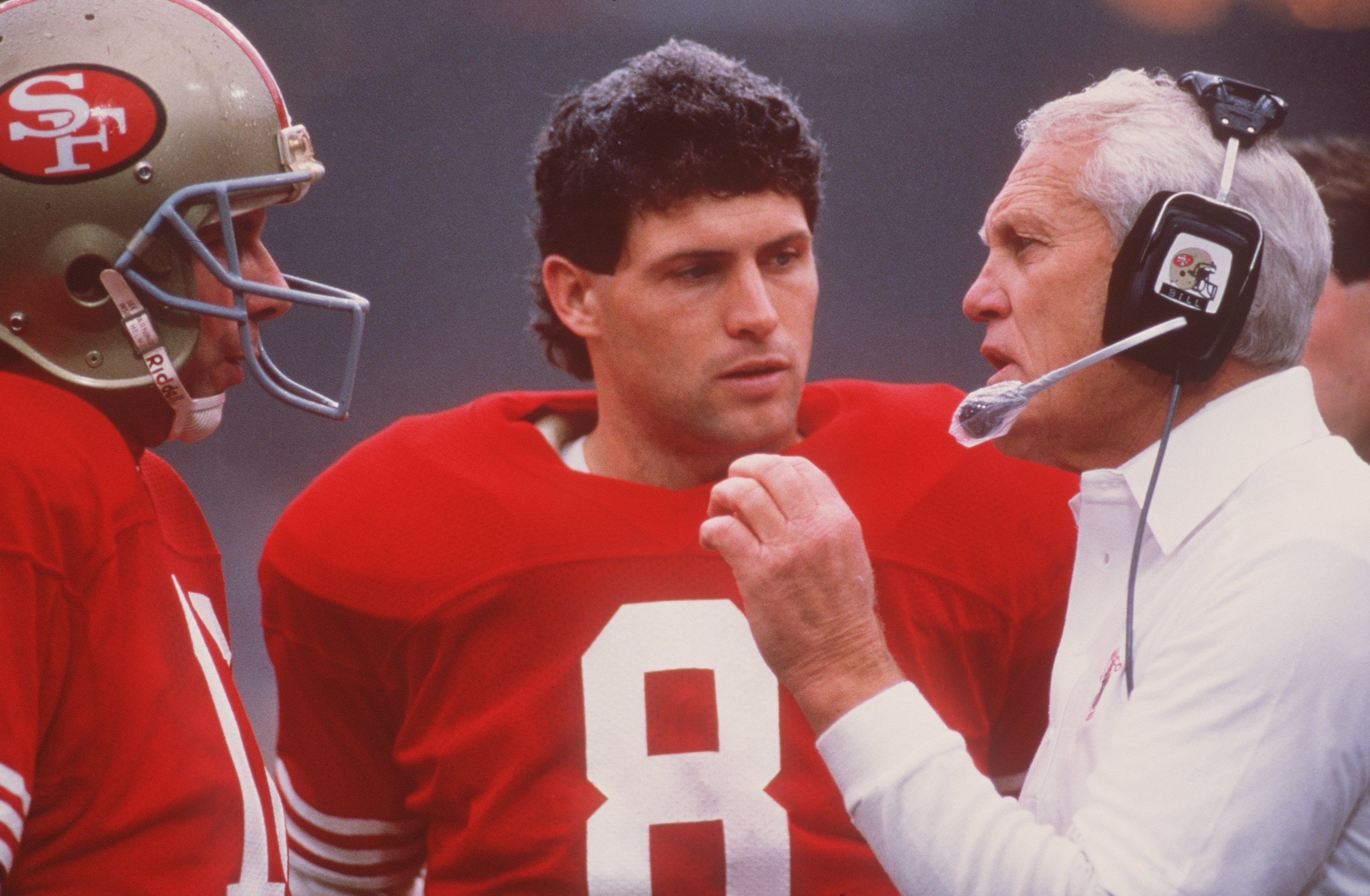 NOV 1987:  SAN FRANCISCO QUARTERBACK JOE MONTANA TALKS WITH HEAD COACH BILL WALSH, AS BACKUP QUARTERBACK STEVE YOUNG LISTENS, DURING THE 49ERS GAME AT CANDLESTICK PARK IN SAN FRANCISCO, CALIFORNIA. Mandatory Credit: Otto Greule/ALLSPORT