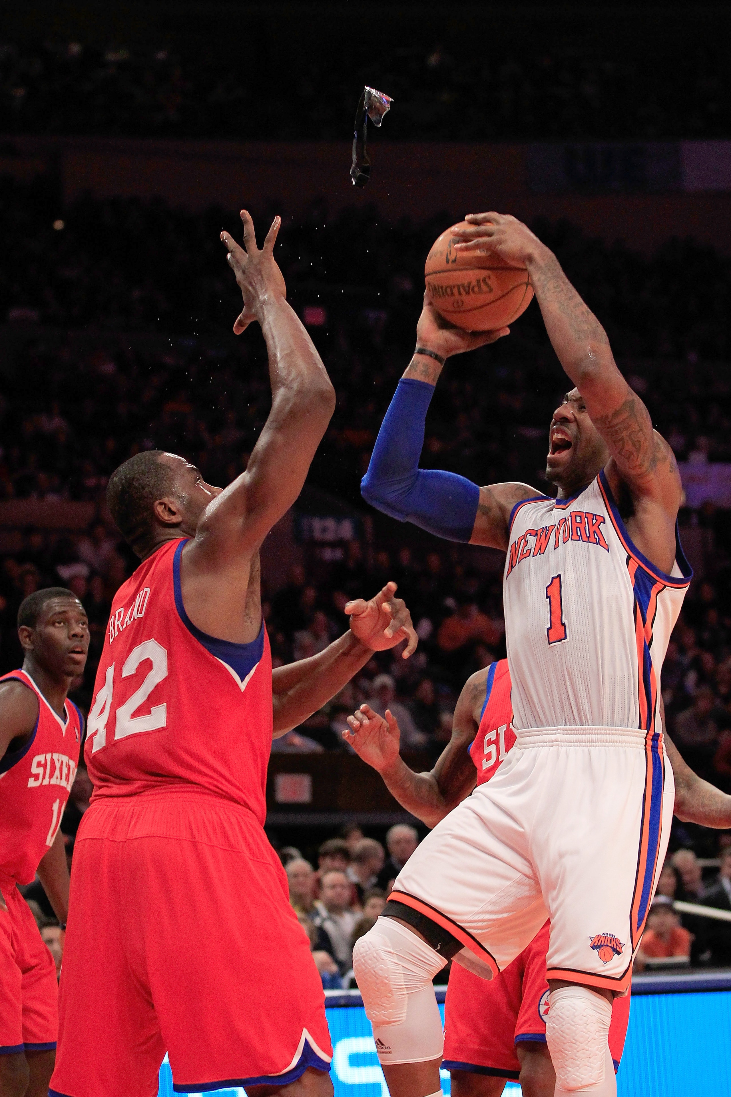 NEW YORK, NY - FEBRUARY 06:  Amar'e Stoudemire #1 of the New York Knicks glasses fly in to the air as he shoots over Elton Brand #42 of the Philadelphia 76ers at Madison Square Garden on February 6, 2011 in New York City. NOTE TO USER: User expressly ackn