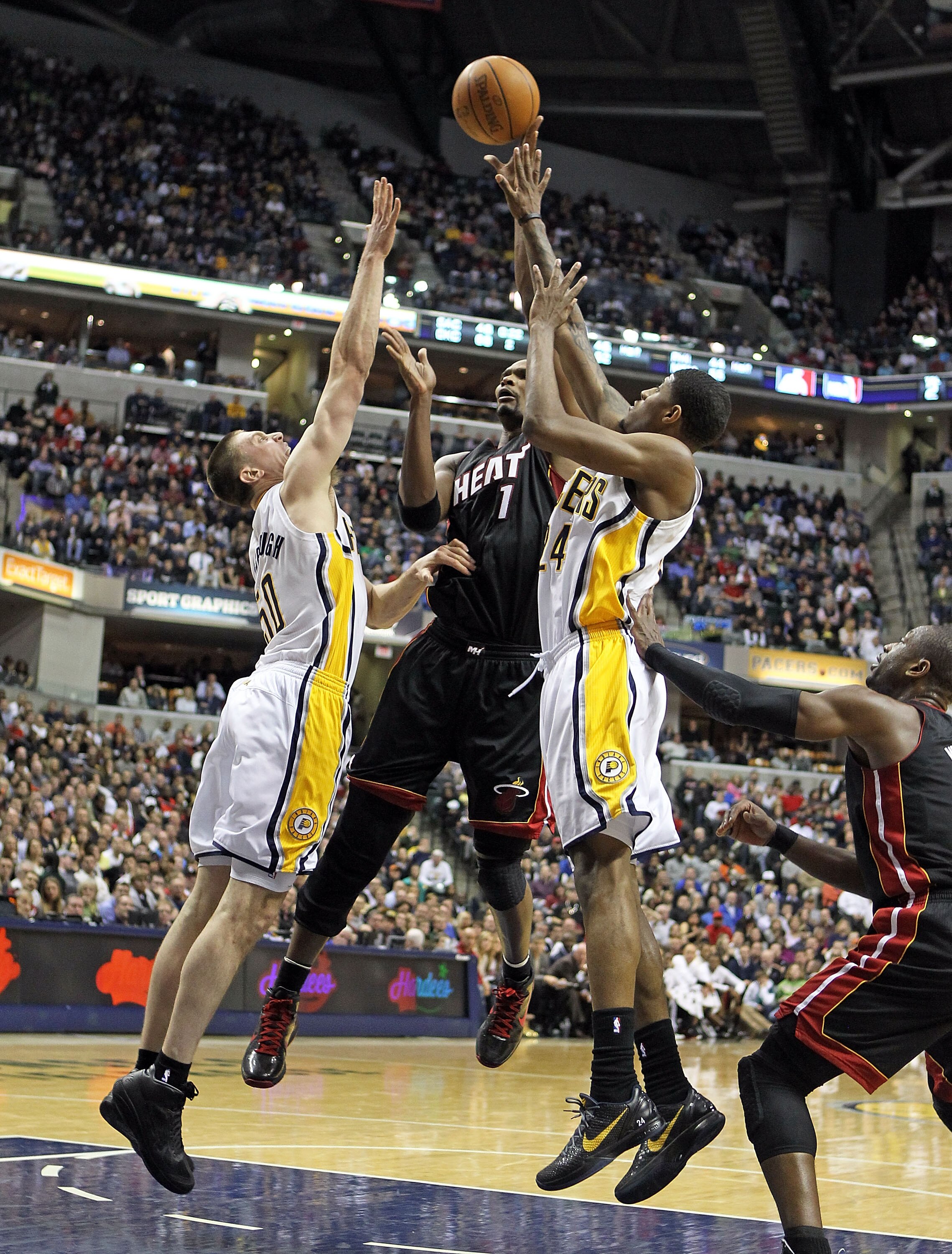 INDIANAPOLIS - FEBRUARY 15:  Chris Bosh #1 of the Miami Heat shoots the ball while defended by Tyler Hansbrough #50 and Paul George #24 of the Indiana Pacers during the NBA game at Conseco Fieldhouse on February 15, 2011 in Indianapolis, Indiana.   The He