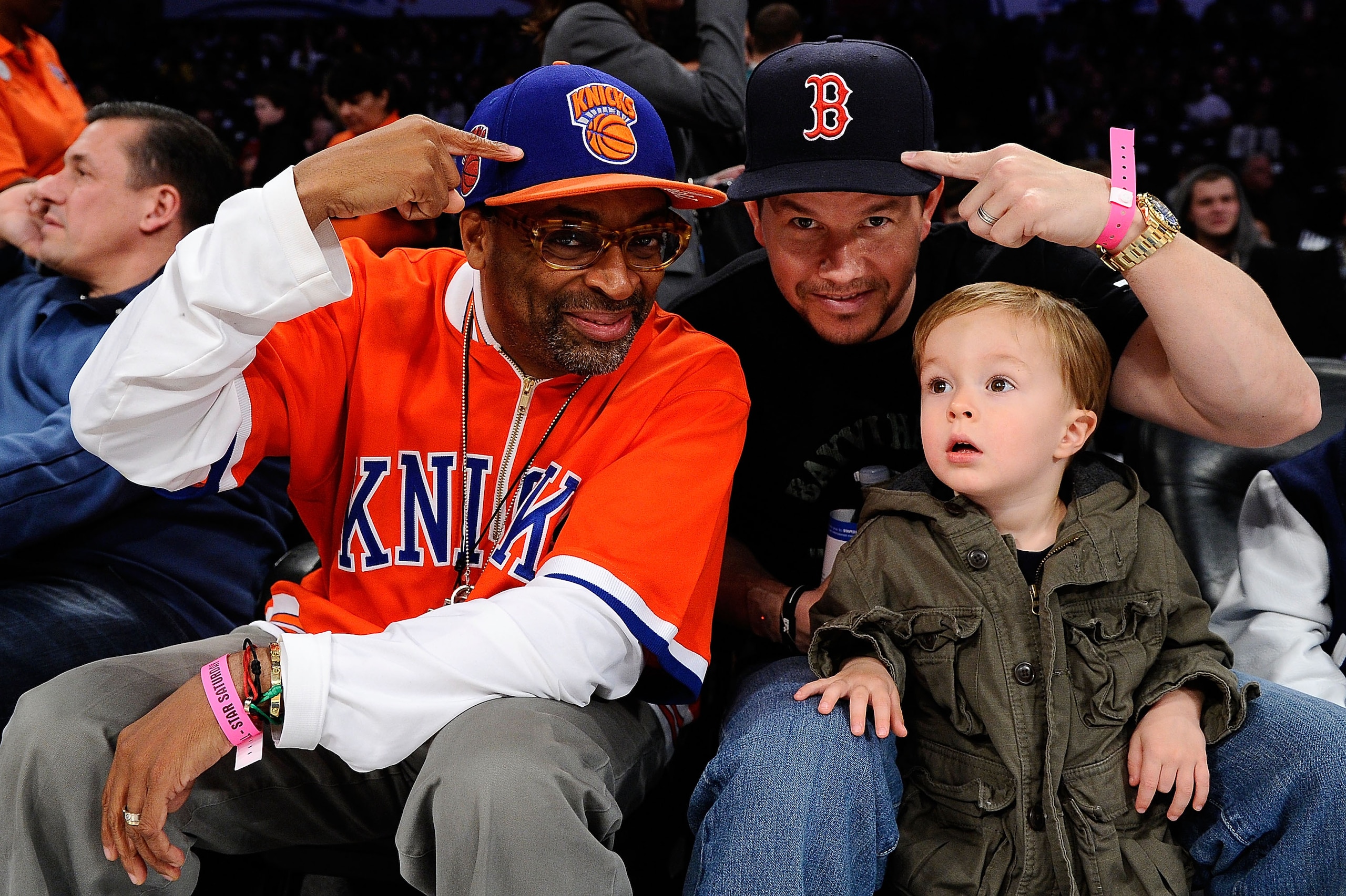 LOS ANGELES, CA - FEBRUARY 19:  Director Spike Lee and actor Mark Wahlberg with son Brendan Walhberg smile as they point at their New York Knicks hat and Boston Red Sox hat respectively during NBA All-Star Saturday night presented by State Farm at Staples