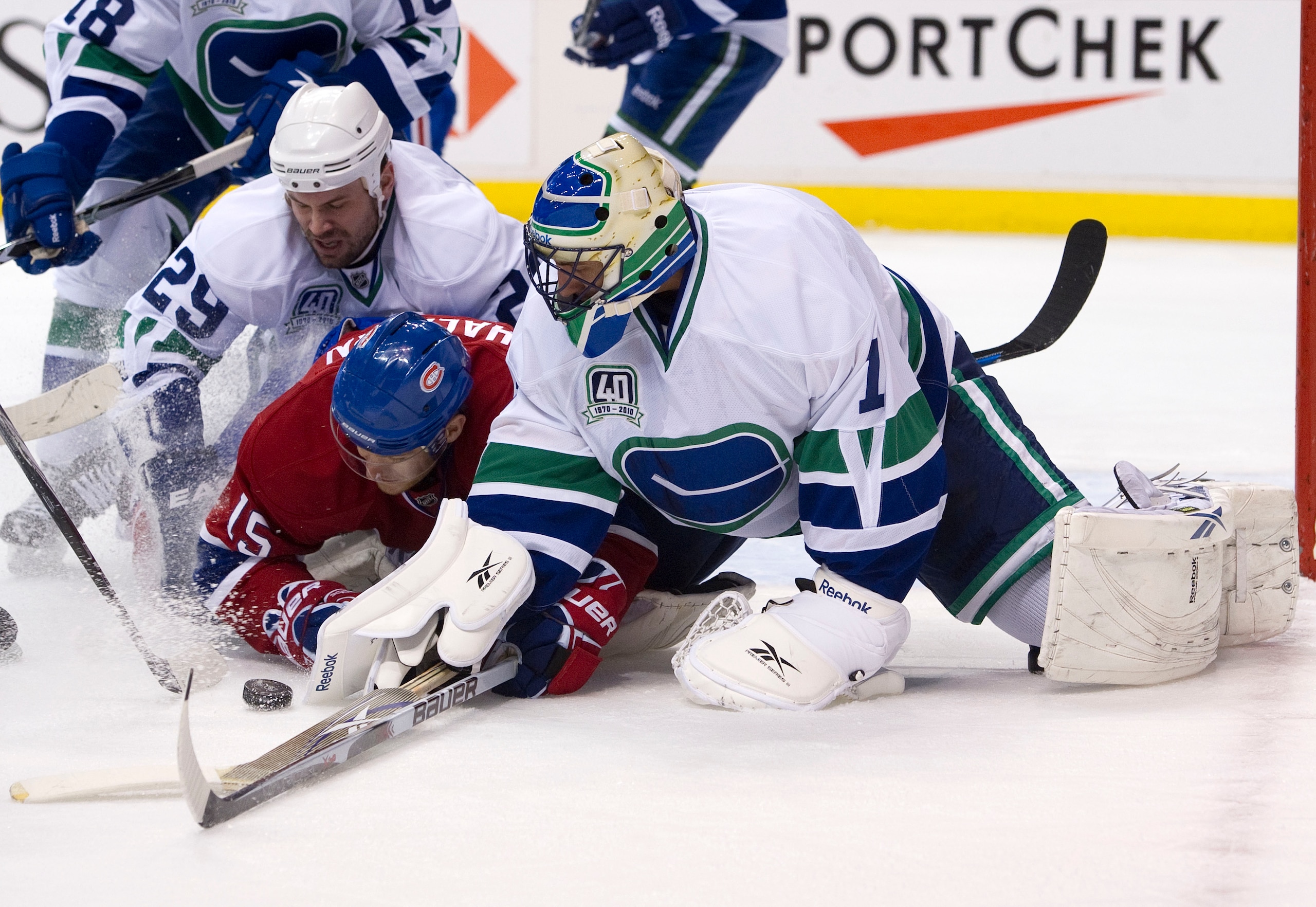 VANCOUVER, CANADA - FEBRUARY 22: Goalie Roberto Luongo #1 of the Vancouver Canucks tries to cover up the loose puck while teammate Aaron Rome #29 ties up Jeff Halpern #15 of the Montreal Canadiens during the first period in NHL action on February 22, 2011