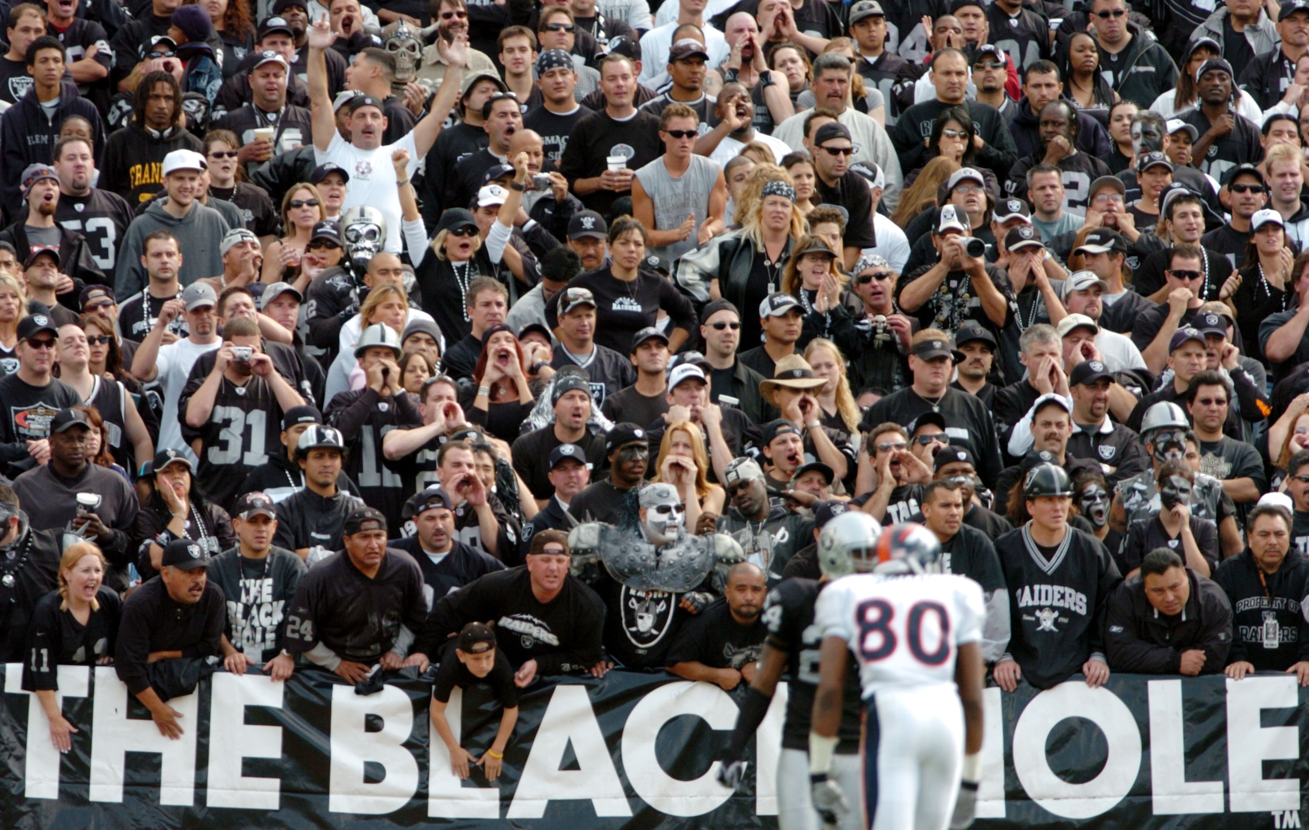 OAKLAND, CA - OCTOBER 17:  Fans in the black hole cheer as Rod Smith #80 of the Denver Broncos and Charles Woodson #24 of the Oakland Raiders line up at scrimmage at the Network Associates Coliseum on October 17, 2004 in Oakland, California.  (Photo by Tr