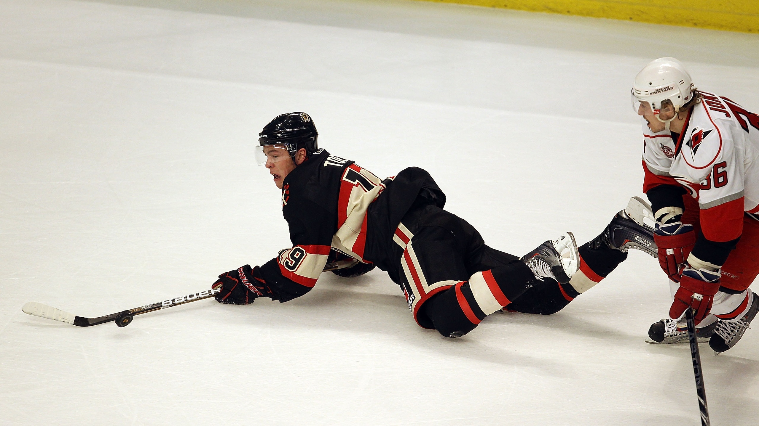 CHICAGO, IL - MARCH 04: Jonathan Toews #19 of the Chicago Blackhawks tries to pass the puck after falling to the ice under pressure from Jussi Jokinen #36 of the Carolina Hurricanes at the United Center on March 4, 2011 in Chicago, Illinois. (Photo by Jon