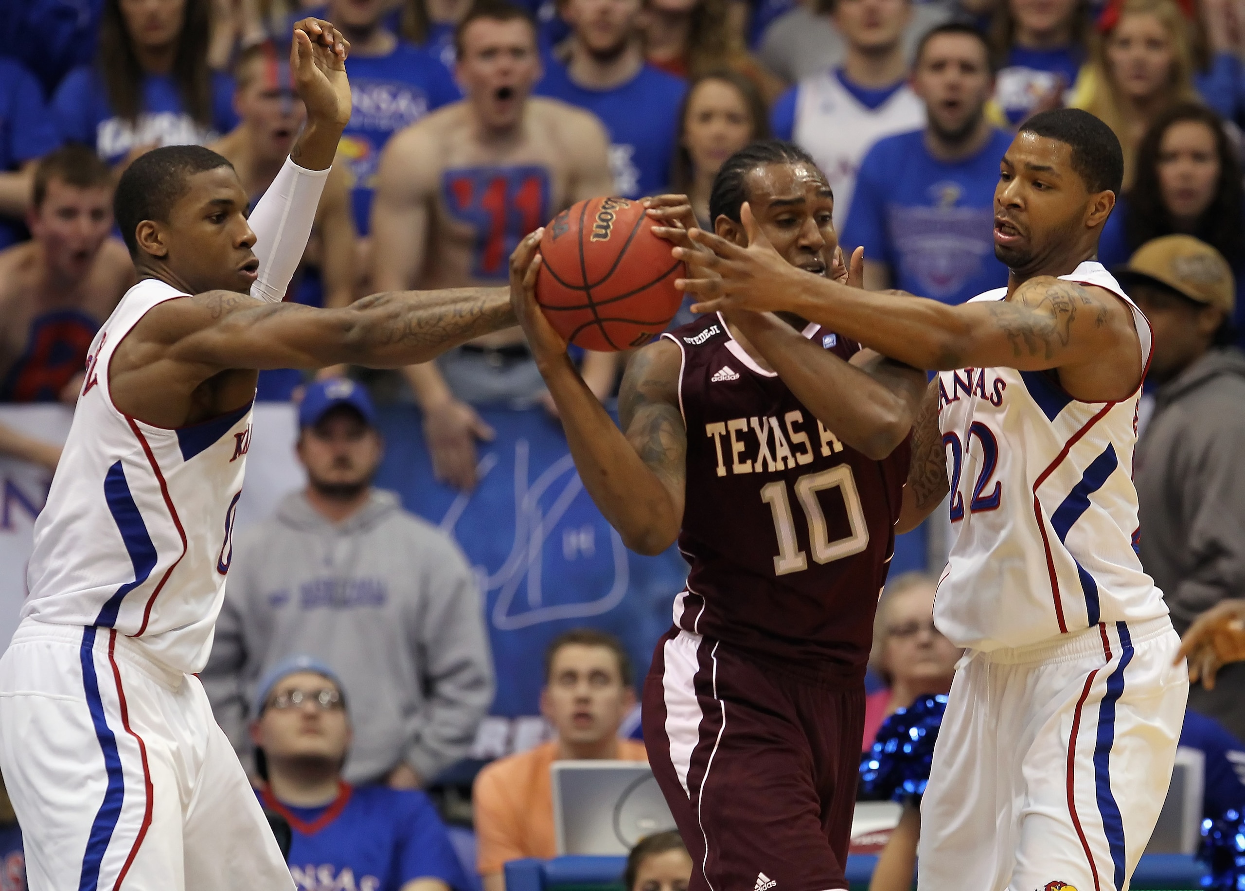 LAWRENCE, KS - MARCH 02:  David Loubeau #10 of the Texas A&M Aggies controls the ball as Thomas Robinson #0 and Marcus Morris #22 of the Kansas Jayhawks defend during the game on March 2, 2011 at Allen Fieldhouse in Lawrence, Kansas.  (Photo by Jamie Squi