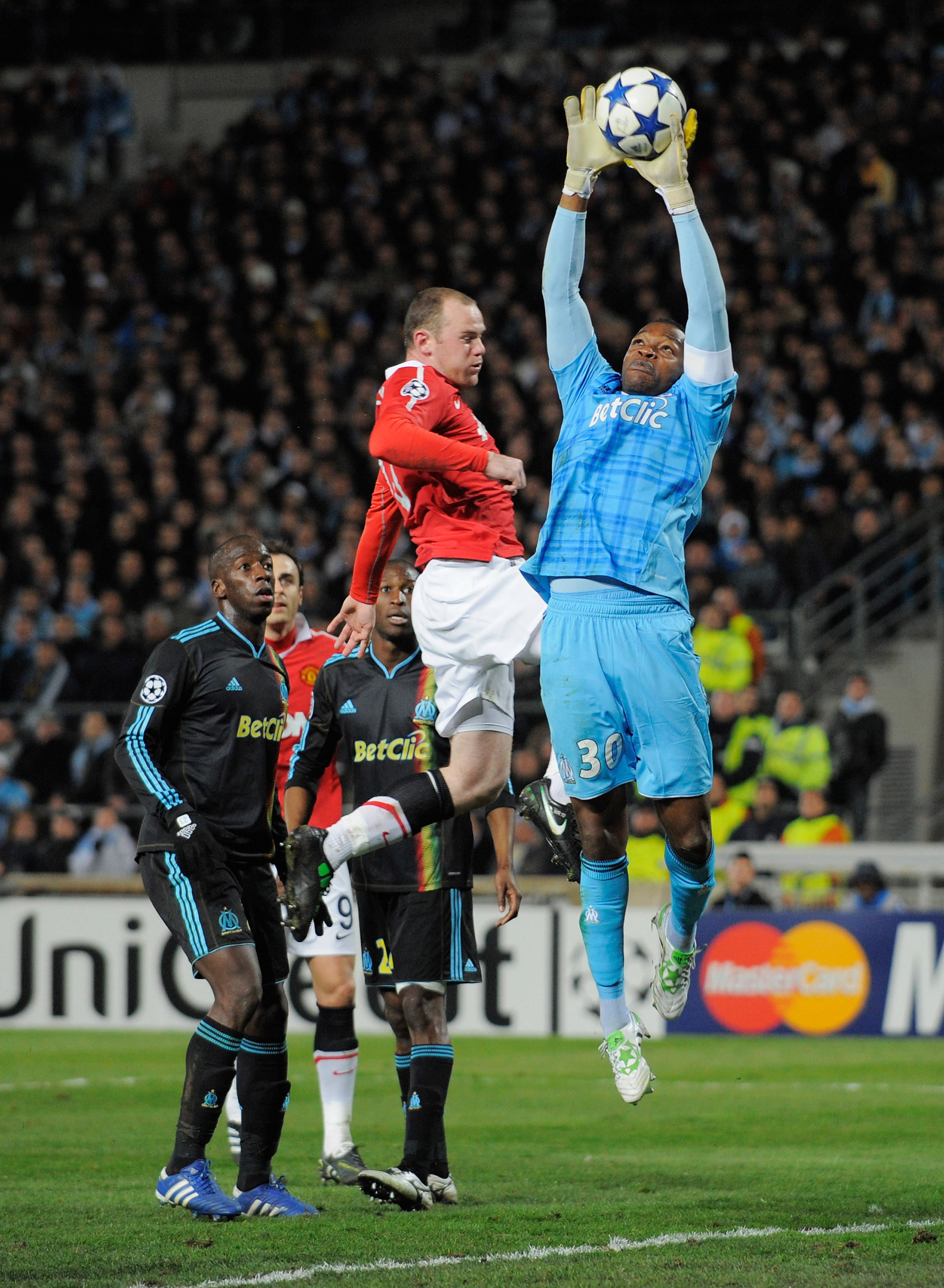 MARSEILLE, FRANCE - FEBRUARY 23:  Steve Mandanda of Marseille claims the ball under a challenge by Wayne Rooney of Manchester United during the UEFA Champions League round of 16 first leg match between Marseille and Manchester United at the Stade Velodrom