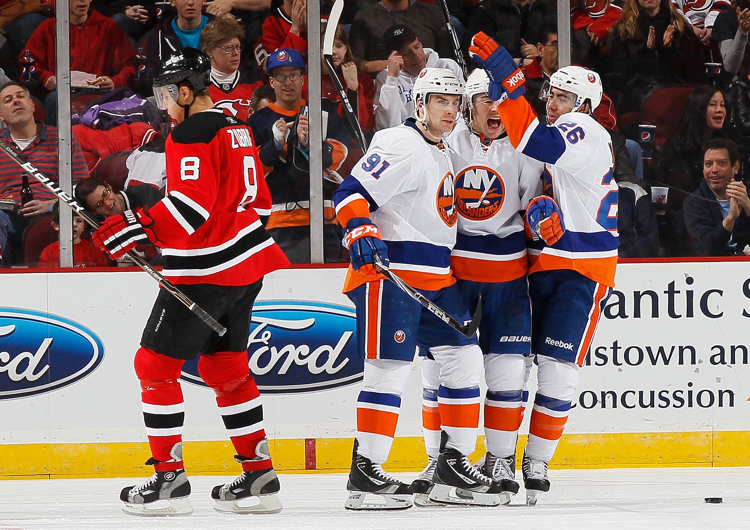 NEWARK, NJ - MARCH 12:  John Tavares #91 of the New York Islanders celebrates his second period goal with teammates Matt Moulson #26 and PA Parenteau #15 as Dainius Zubrus #8 of the New Jersey Devils skates away dejected on March 12, 2011 at the Prudentia