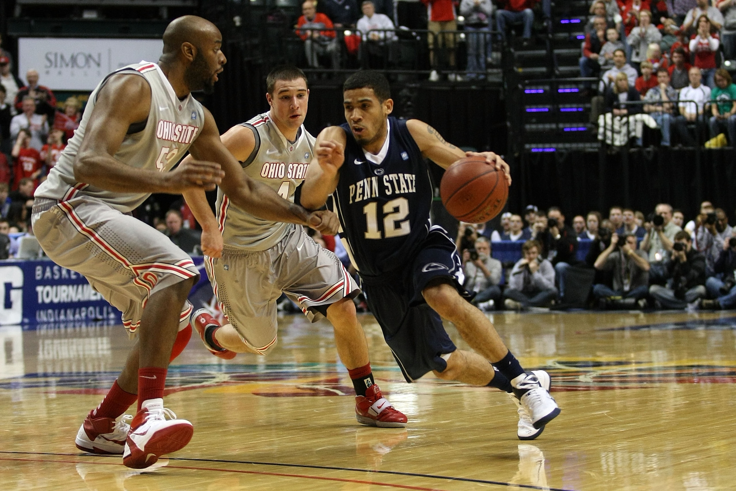 INDIANAPOLIS, IN - MARCH 13:  Talor Battle #12 of the Penn State Nittany Lions drives against Dallas Lauderdale #52 and Aaron Craft #4 of the Ohio State Buckeyes during the championship game of the 2011 Big Ten Men's Basketball Tournament at Conseco Field