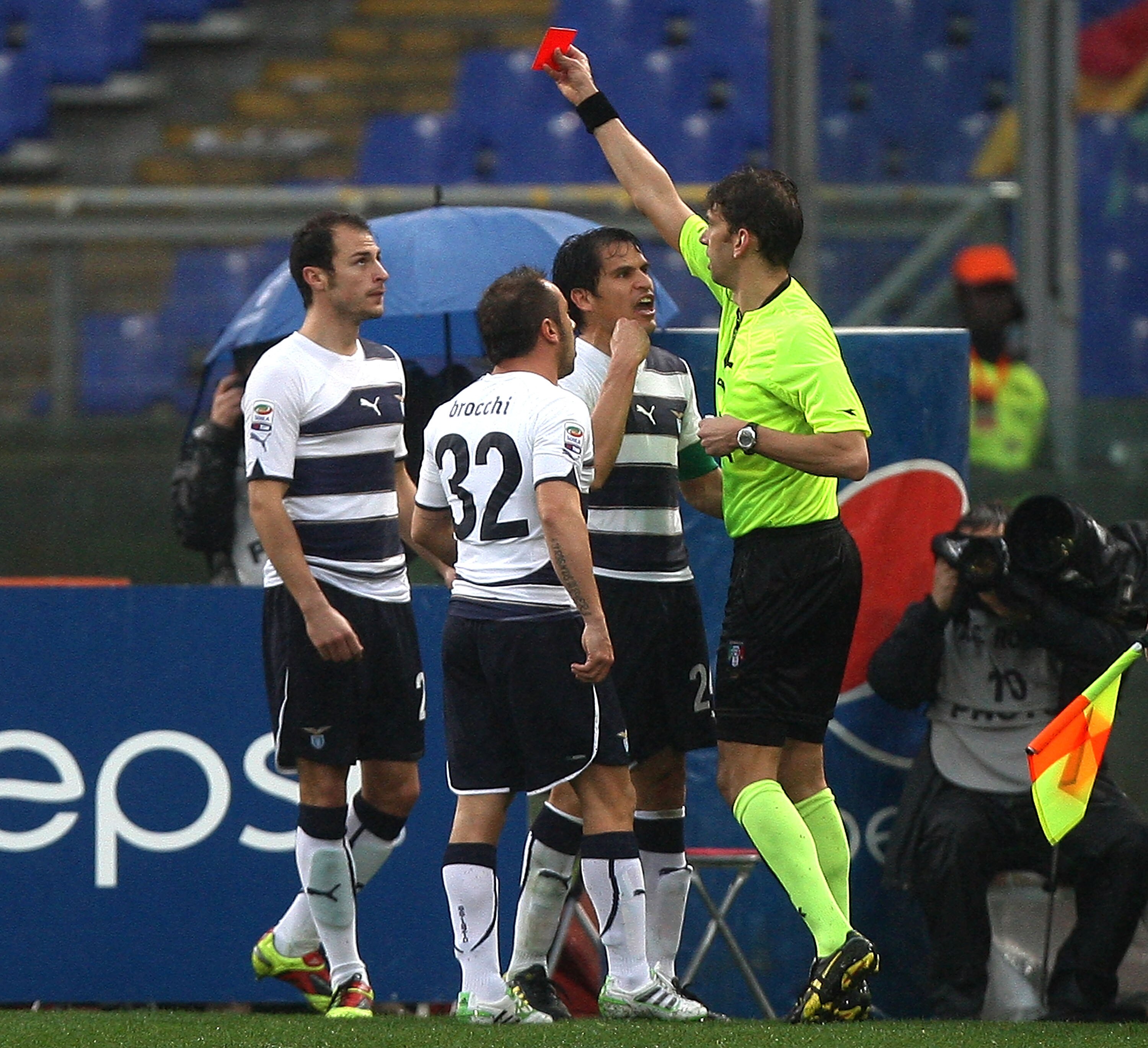 ROME, ITALY - MARCH 13:  The referee Paolo Tagliavento shows the red card to Stephan Radu (L) of SS Lazio as his teammates Cristian Brocchi #32 and Cristian Ledesma (2ndR) react during Serie A match between AS Roma and SS Lazio at Stadio Olimpico on March