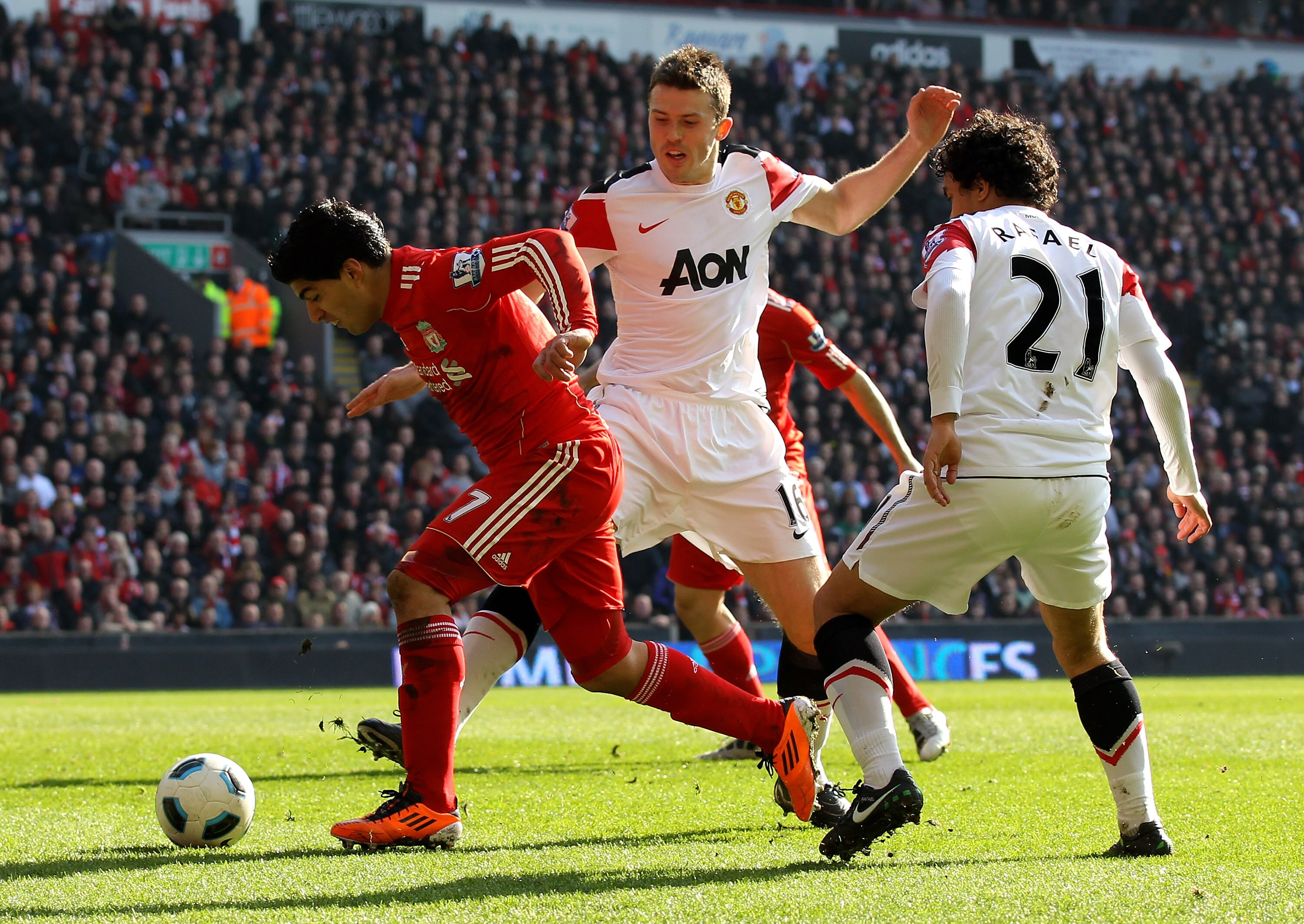 LIVERPOOL, ENGLAND - MARCH 06:  Luis Suarez of Liverpool goes clear of Michael Carrick and Rafael (R) of Manchester United to set up the first goal during the Barclays Premier League match between Liverpool and Manchester United at Anfield on March 6, 201
