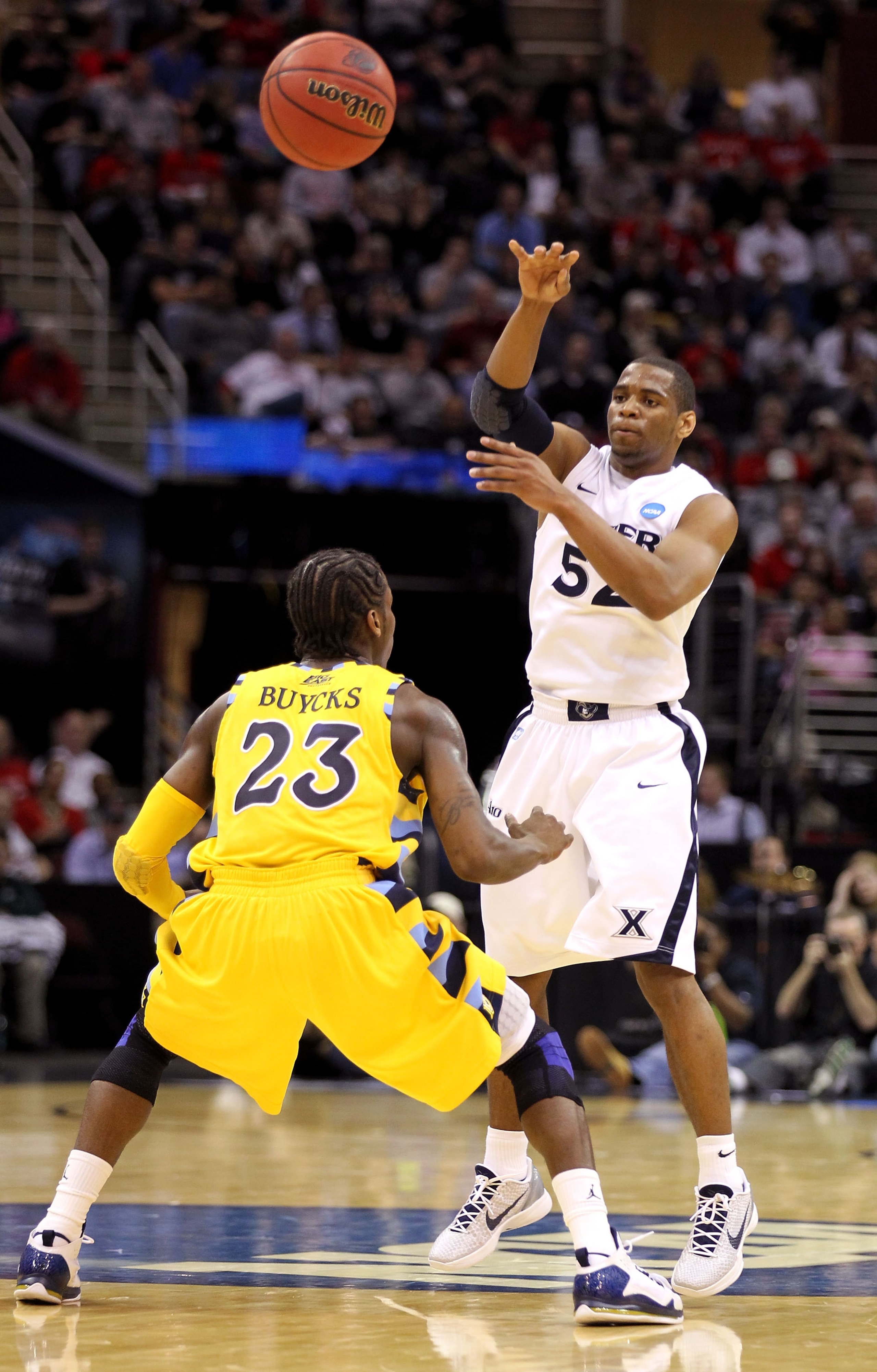 CLEVELAND, OH - MARCH 18: Tu Holloway #52 of the Xavier Musketeers passes over Dwight Buycks #23 of the Marquette Golden Eagles during the second round of the 2011 NCAA men's basketball tournament at Quicken Loans Arena on March 18, 2011 in Cleveland, Ohi