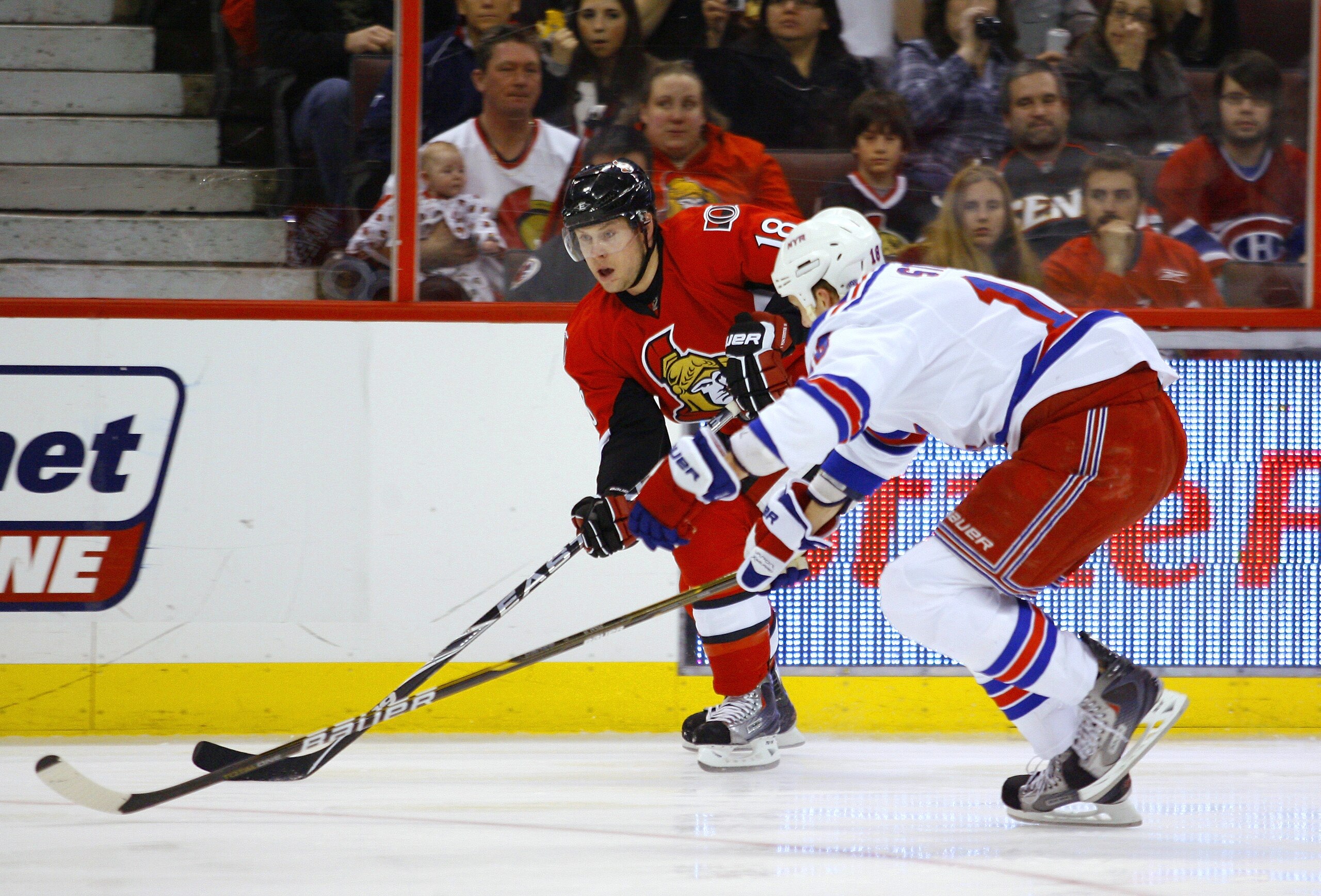 OTTAWA, CANADA - MARCH 04:  Jesse Winchester #18 of the Ottawa Senators carries the puck along the far boards while being checked closely by Marc Staal #18 of the New York Rangers in a game at Scotiabank Place on March 4, 2011 in Ottawa, Ontario, Canada.