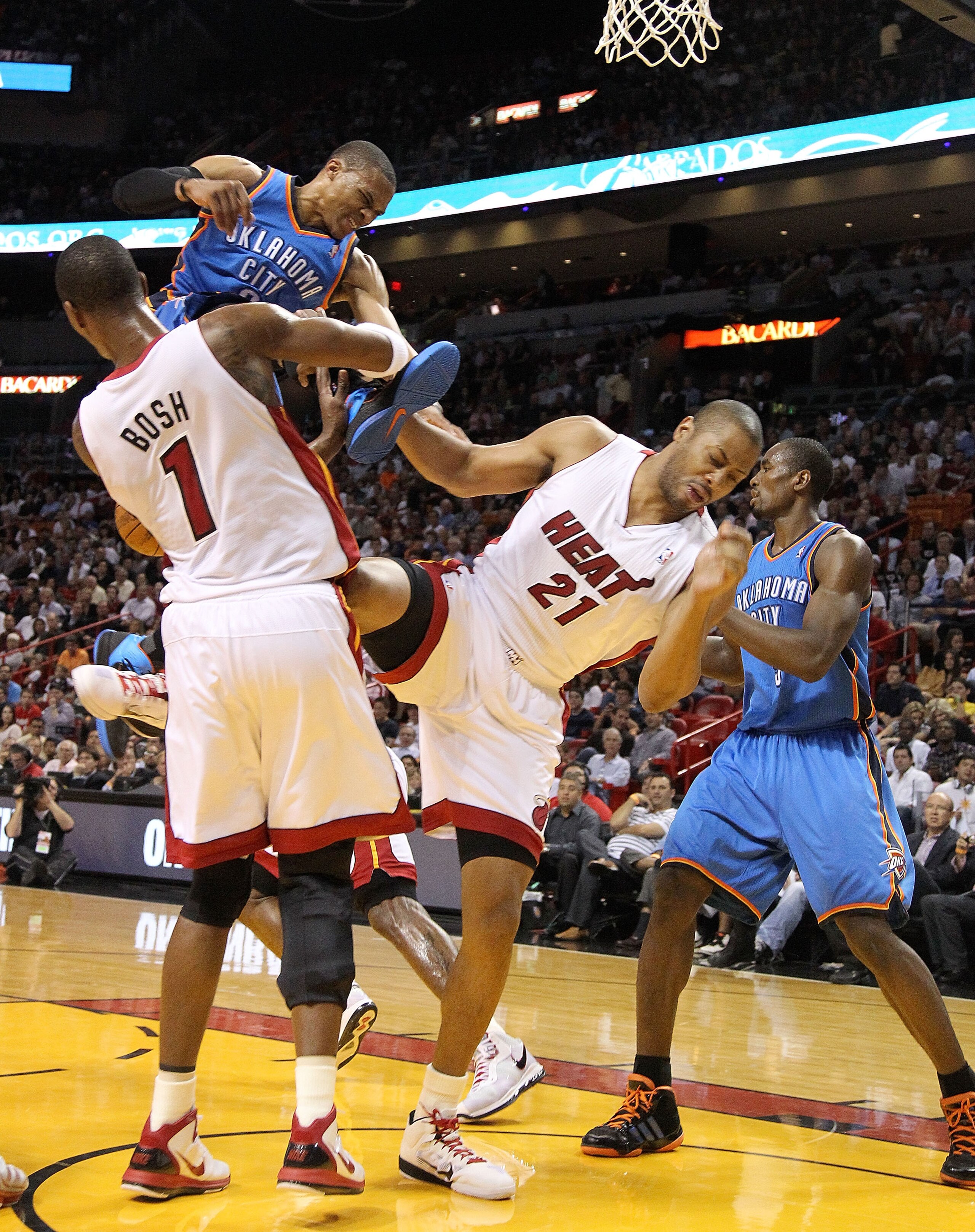 MIAMI, FL - MARCH 16:  Russell Wetbrook #0  of the the Oklahoma City Thunder collides with Jamaal Magloire #21 and Chris Bosh #1 of the Miami Heat during a game at American Airlines Arena on March 16, 2011 in Miami, Florida. NOTE TO USER: User expressly a
