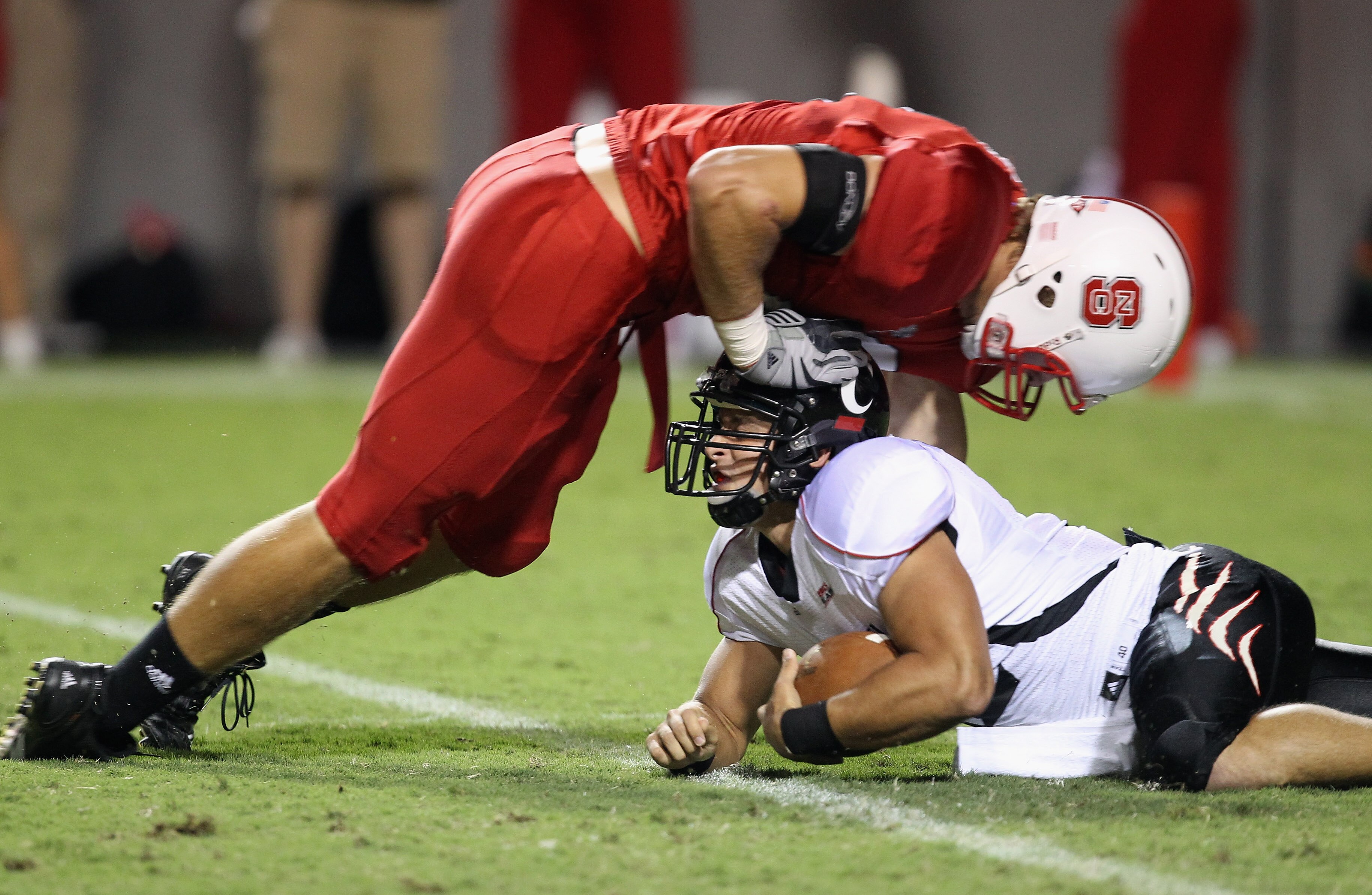 RALEIGH, NC - SEPTEMBER 16:  Zack Collaros #12 of the Cincinnati Bearcats is tackled by Audie Cole #42 of the North Carolina State Wolfpack after recovering a fumble during their game at Carter-Finley Stadium on September 16, 2010 in Raleigh, North Caroli