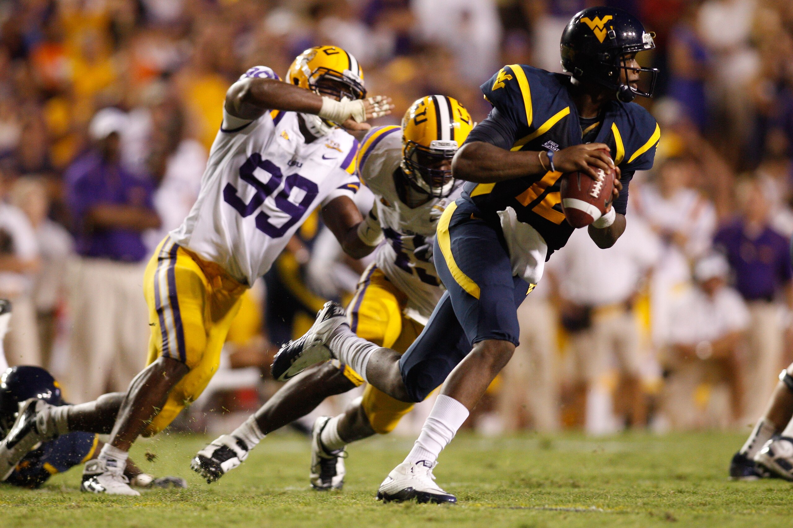 BATON ROUGE, LA - SEPTEMBER 25:  Quarterback Geno Smith #12 of the West Virginia Mountaineers avoids a tackle by Sam Montgomery #99 of the  Louisiana State University Tigers at Tiger Stadium on September 25, 2010 in Baton Rouge, Louisiana.  The Tigers def