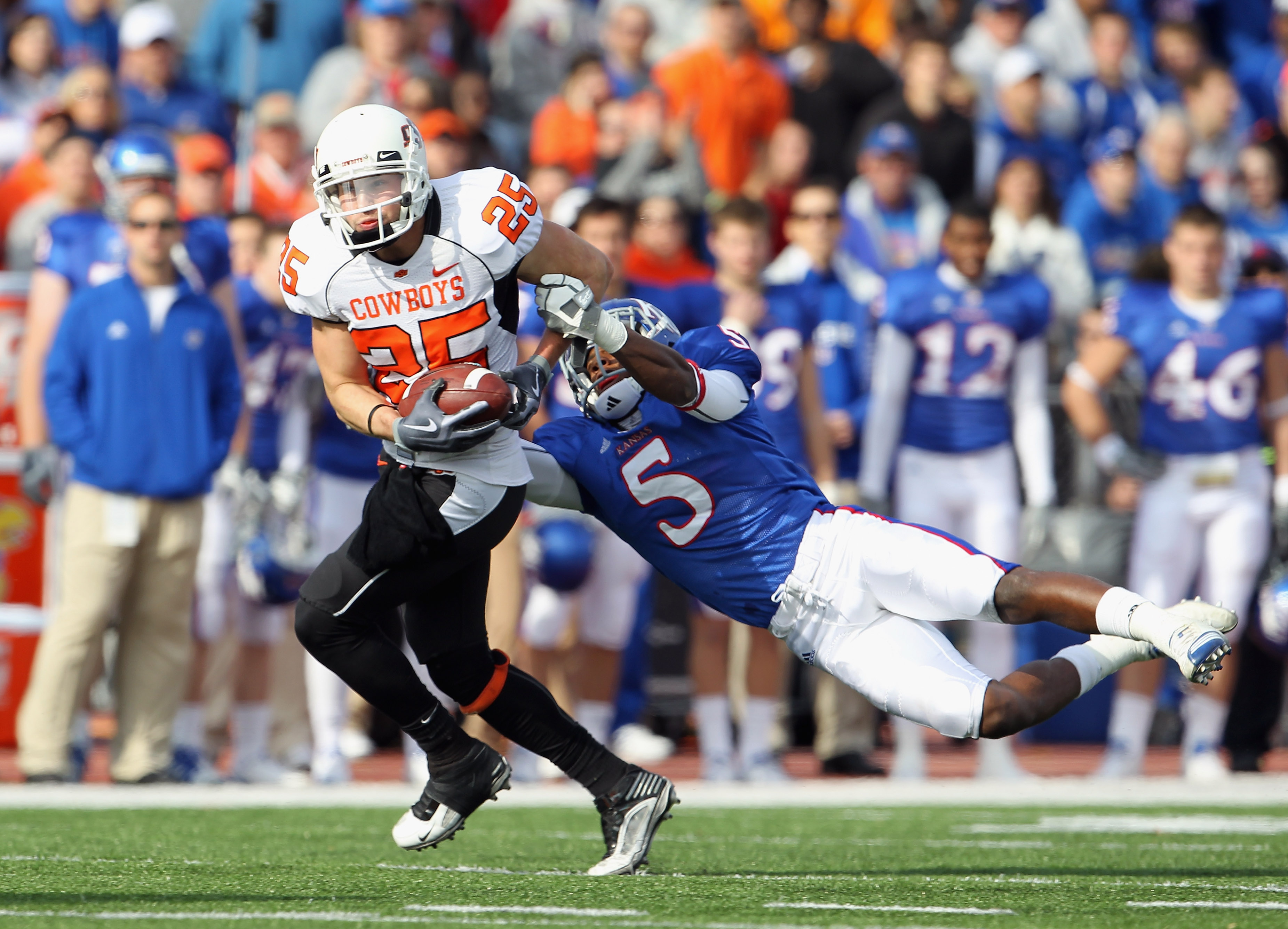 LAWRENCE, KS - NOVEMBER 20: Josh Cooper #25 of the Oklahoma State Cowboys carries the ball as Greg Brown #5 of the Kansas Jayhawks defends during the game on November 20, 2010 at Memorial Stadium in Lawrence, Kansas. (Photo by Jamie Squire/Getty Images)