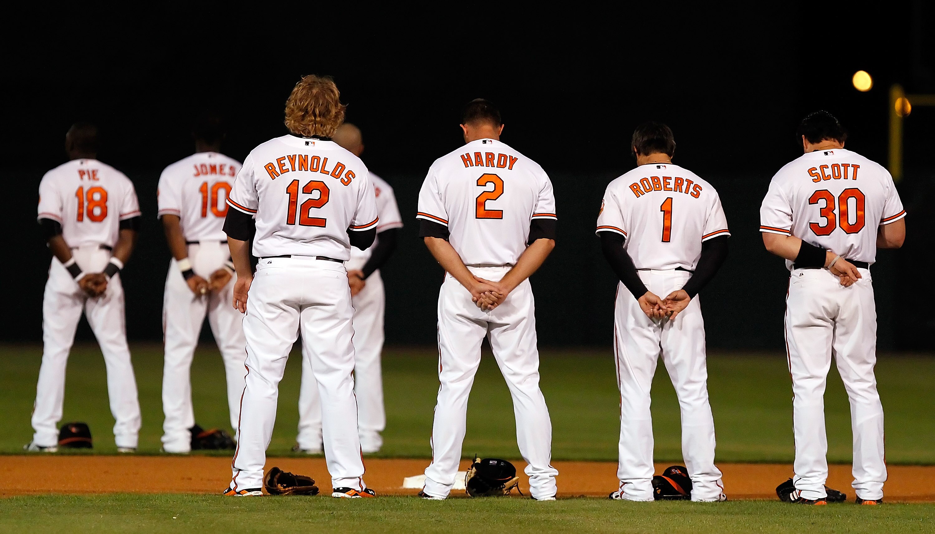SARASOTA, FL - MARCH 07:  Infielders Mark Reynolds #12, J.J. Hardy #2, Brian Roberts #1 and Luke Scott #30 of the Baltimore Orioles bow their heads for the National Anthem just before the start of the Grapefruit League Spring Training Game against the New