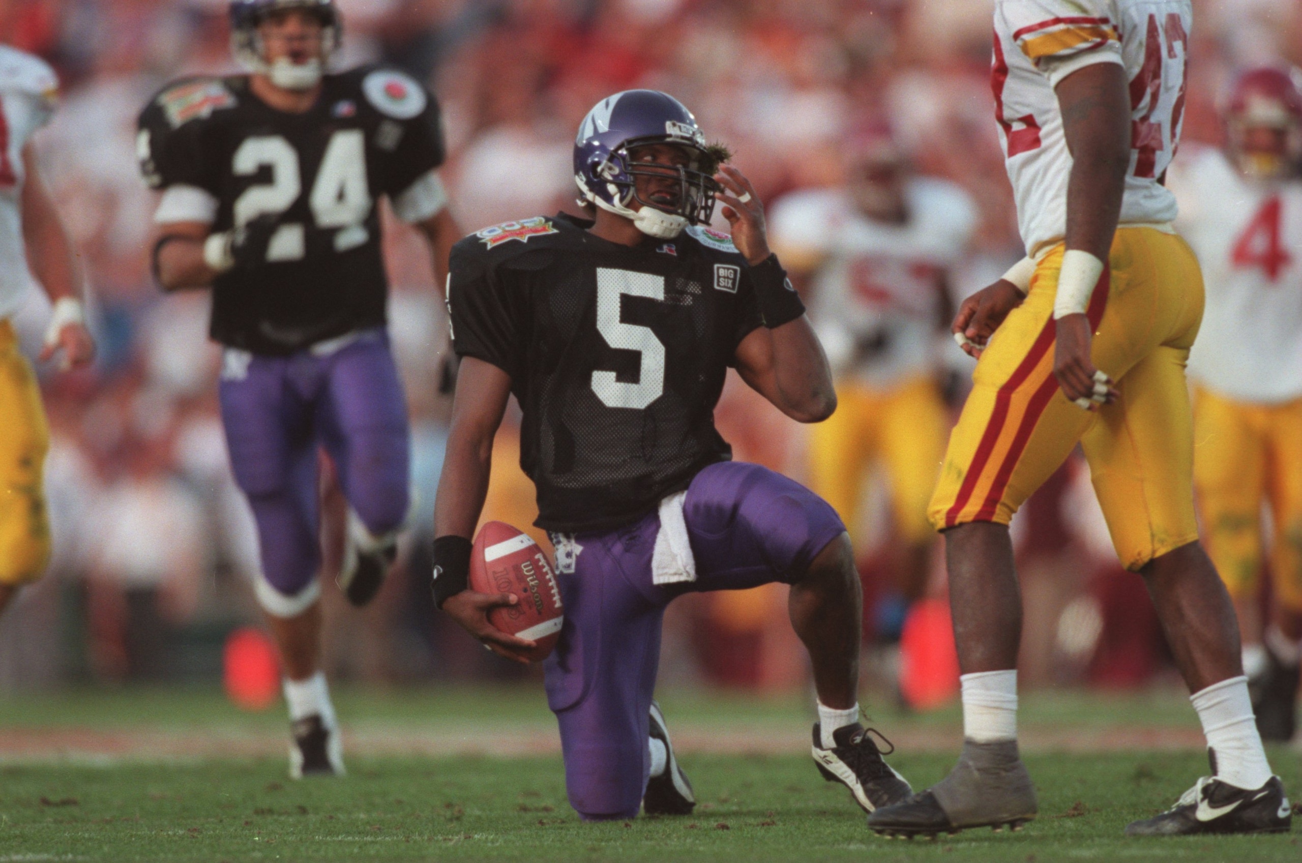 1 Jan 1996:  Running back D'Wayne Bates #5 of the Northwestern Wildcats reaches for his helmet as he attempts to remove a clump of grass from his face mask following a carry in the Wildcats 41-32 loss to the USC Trojans in the 1996 Rose Bowl game held at