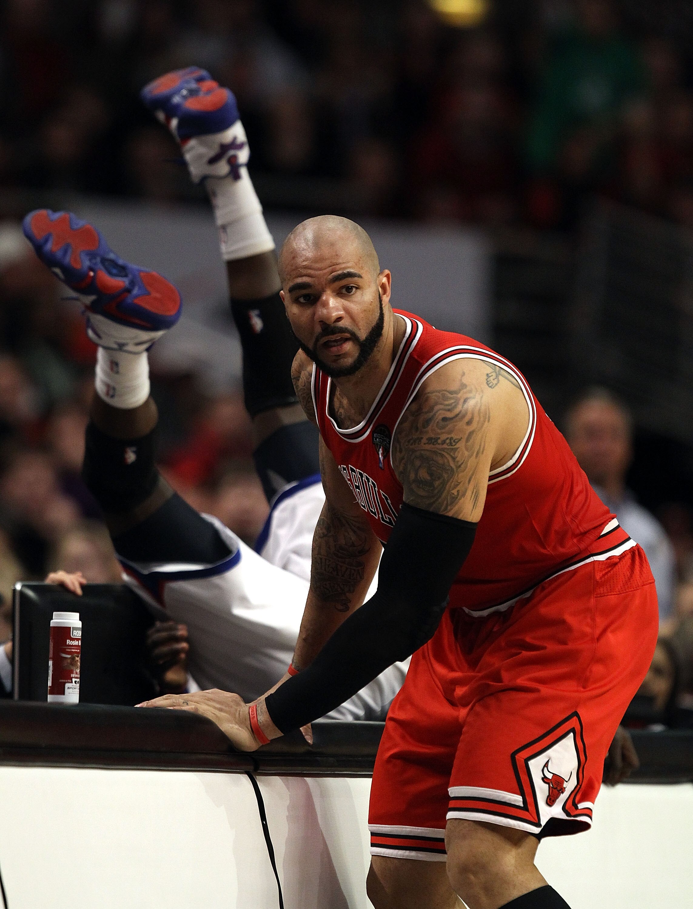 CHICAGO, IL - MARCH 28: Carlos Boozer #5 of the Chicago Bulls stops at the scorer's table as Jrue Holiday #11 of the Philadelphia 76ers flips over the edge at the United Center on March 28, 2011 in Chicago, Illinois. The 76ers defeated the Bulls 97-85. NO