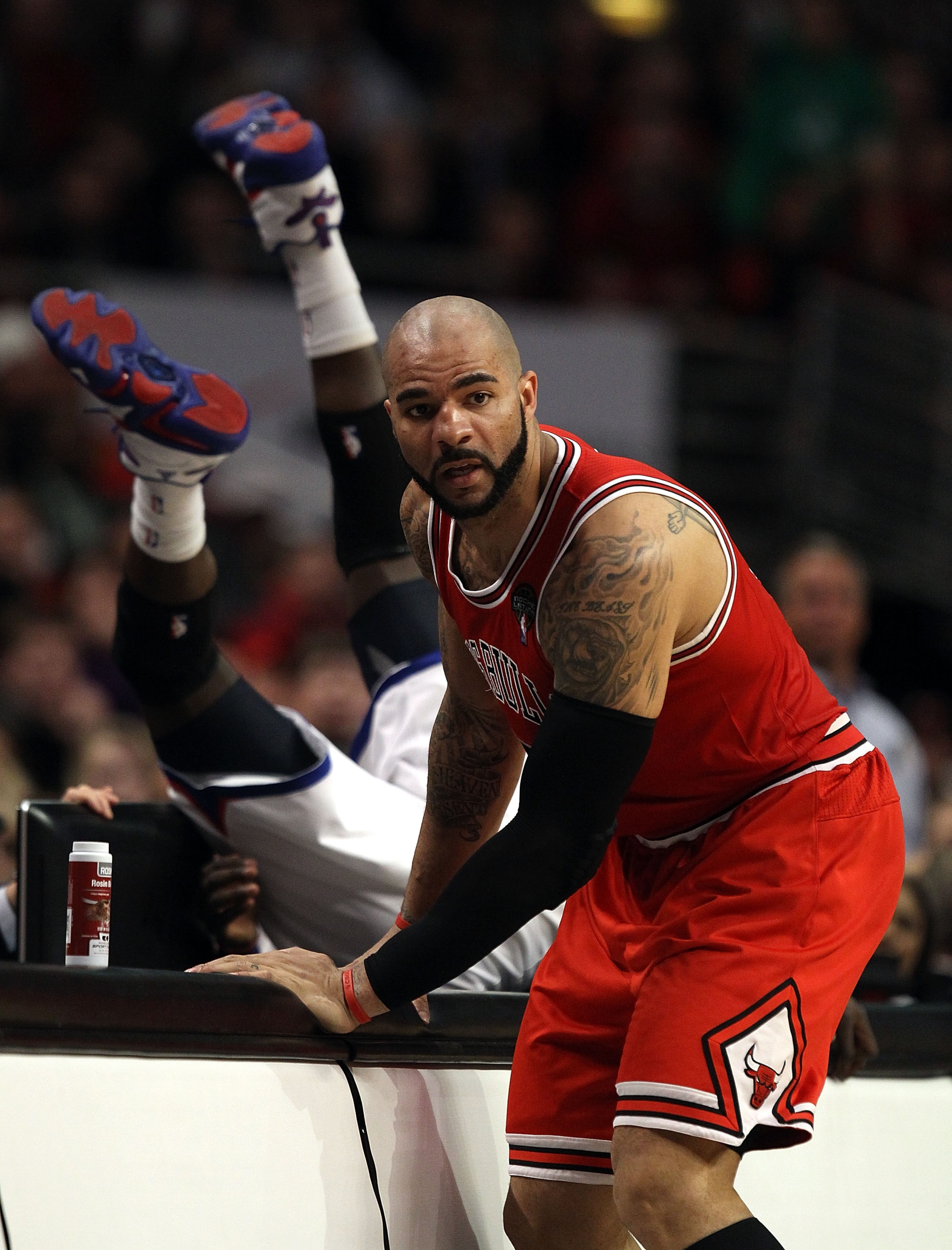 CHICAGO, IL - MARCH 28: Carlos Boozer #5 of the Chicago Bulls stops at the scorer's table as Jrue Holiday #11 of the Philadelphia 76ers flips over the edge at the United Center on March 28, 2011 in Chicago, Illinois. The 76ers defeated the Bulls 97-85. NO