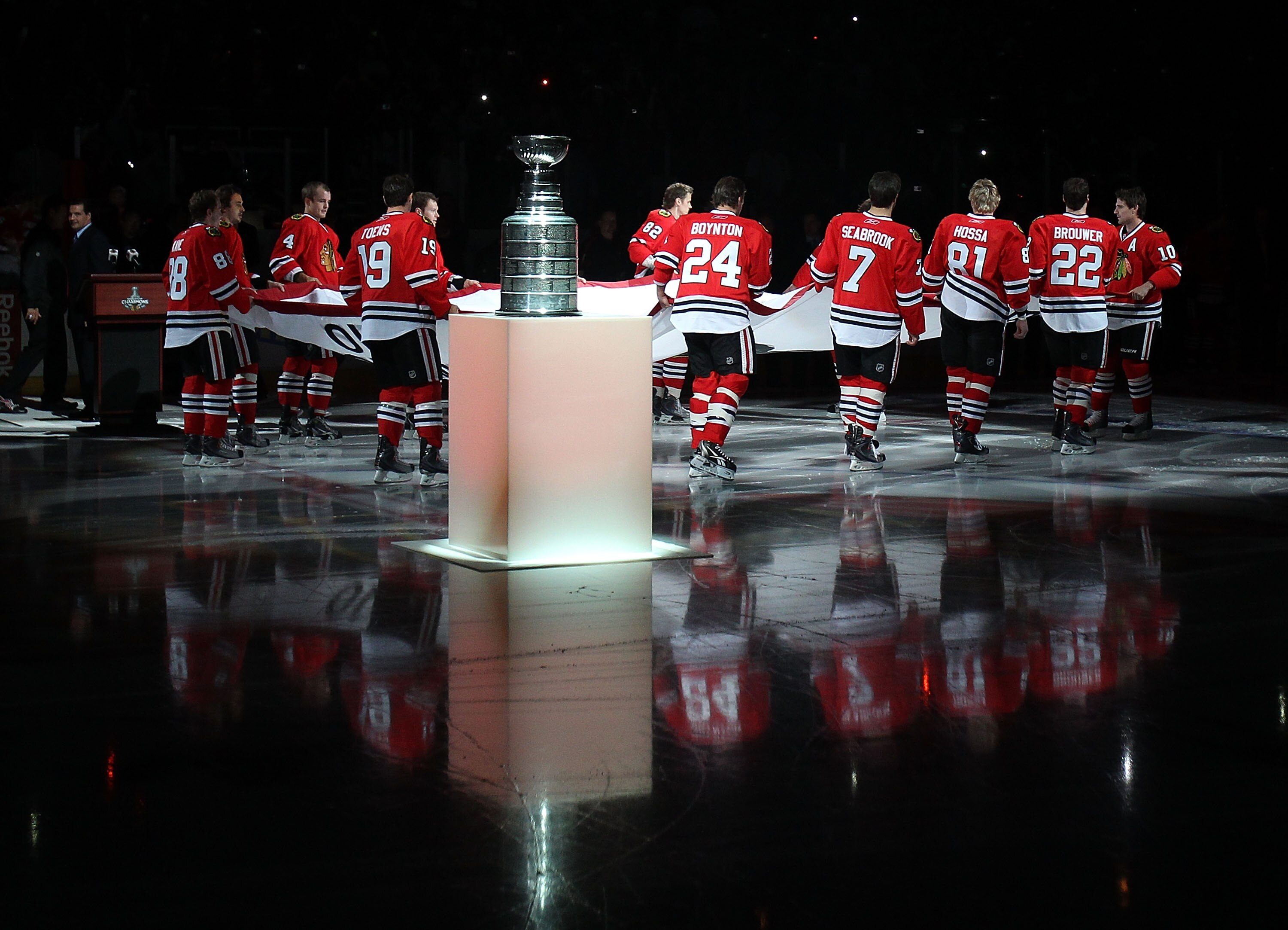 CHICAGO - OCTOBER 09: Members of the Chicago Blackhawks carry the Stanley Cup Championship banner across the ice past the Stanley Cup in a ceremony before the Blackhawks season home opening game against the Detroit Red Wings at the United Center on Octobe