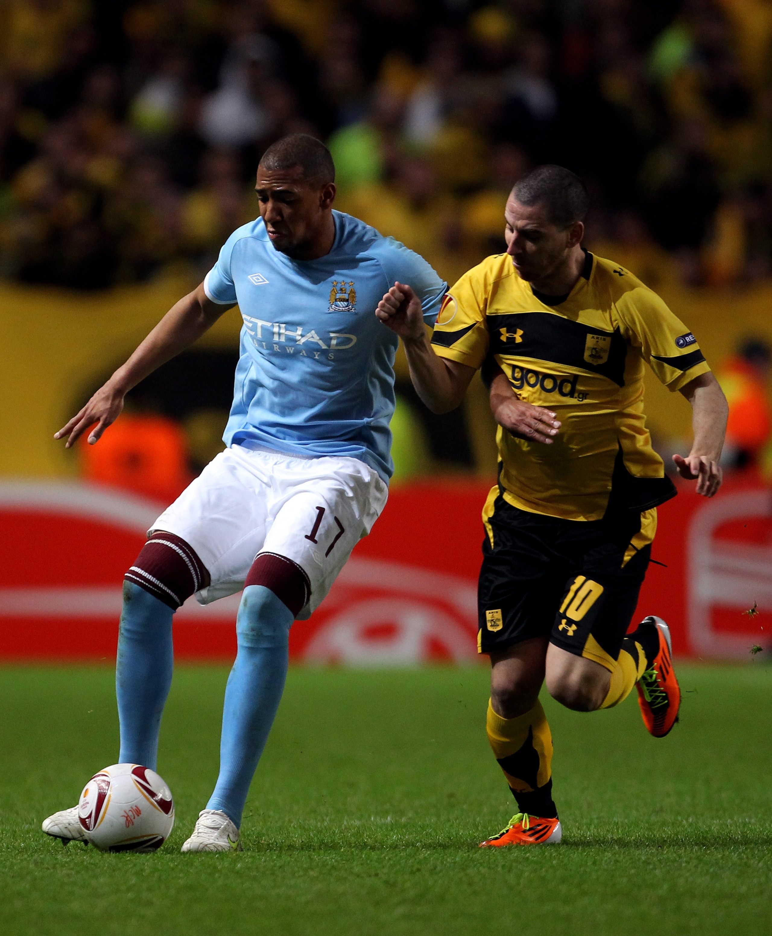 MANCHESTER, ENGLAND - FEBRUARY 24:  Jerome Boateng (L) of City holds off the challenge of Sergio Pardo of Selonika during the UEFA Europa League round of 32 second leg match between Manchester City and Aris Saloniki at City of Manchester Stadium on Februa