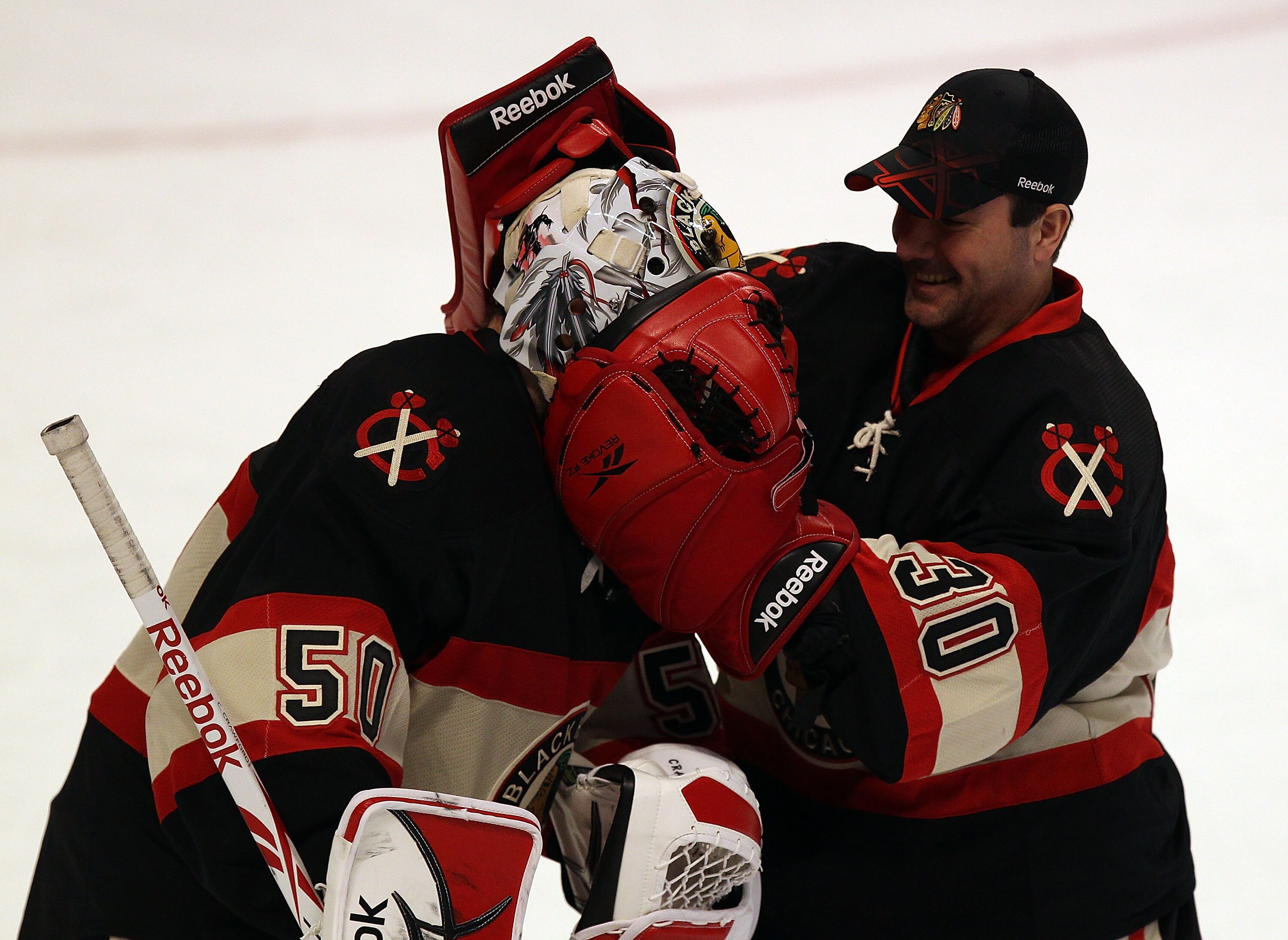 CHICAGO, IL - JANUARY 12: Marty Turco #30 of the Chicago Blackhawks playfully puts his gloves around the head of teammate Corey Crawford #50 who recorded his second straight shut-out in a win over the Colorado Avalanche at the United Center on January 12,