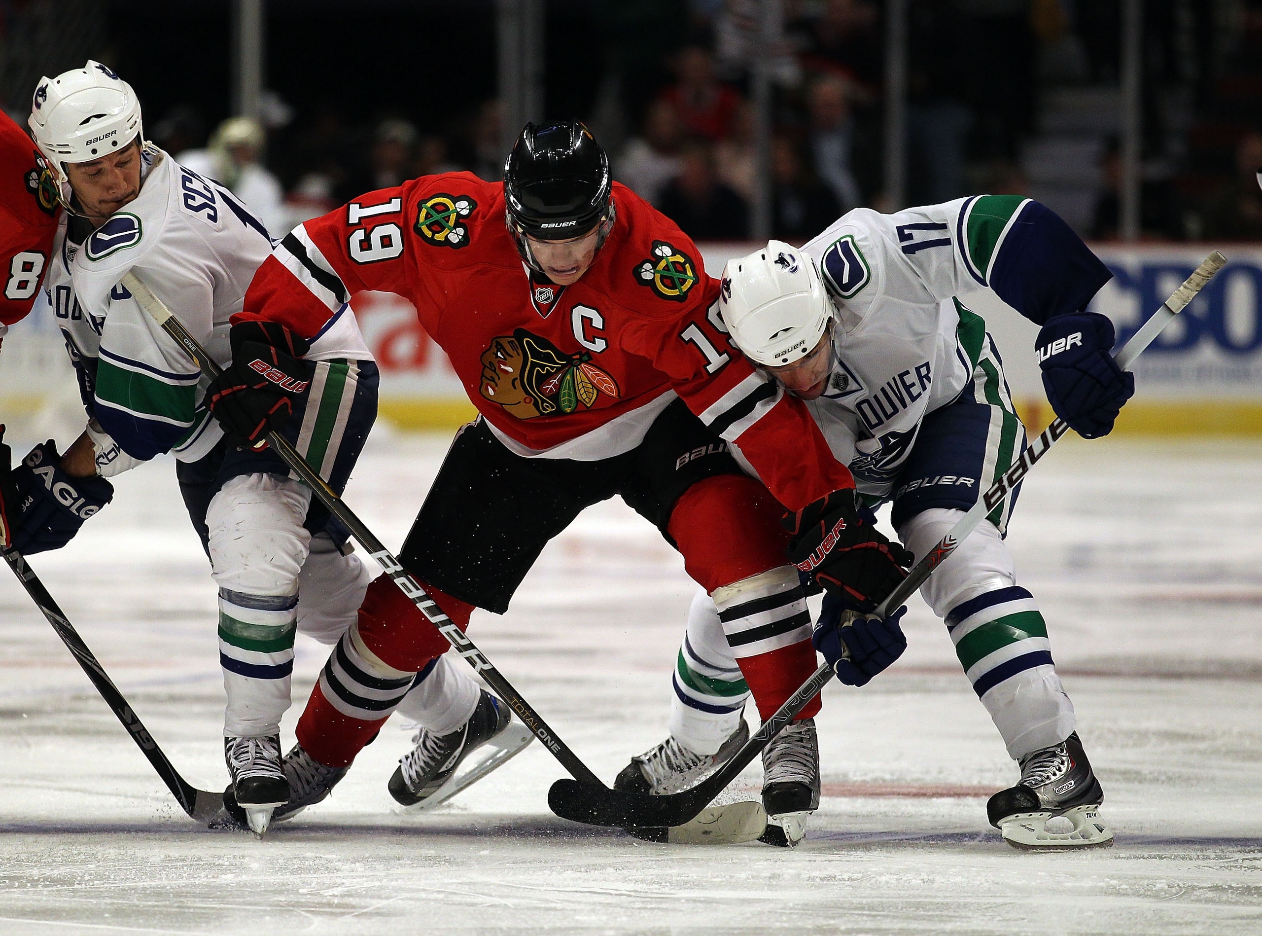 CHICAGO - OCTOBER 20: Jonathan Toews #19 of the Chicago Blackhawks battles for the puck with Peter Schaefer #18 (L) and Ryan Kesler #17 of the Vancouver Canucks at the United Center on October 20, 2010 in Chicago, Illinois. The Blackhawks defeated the Can