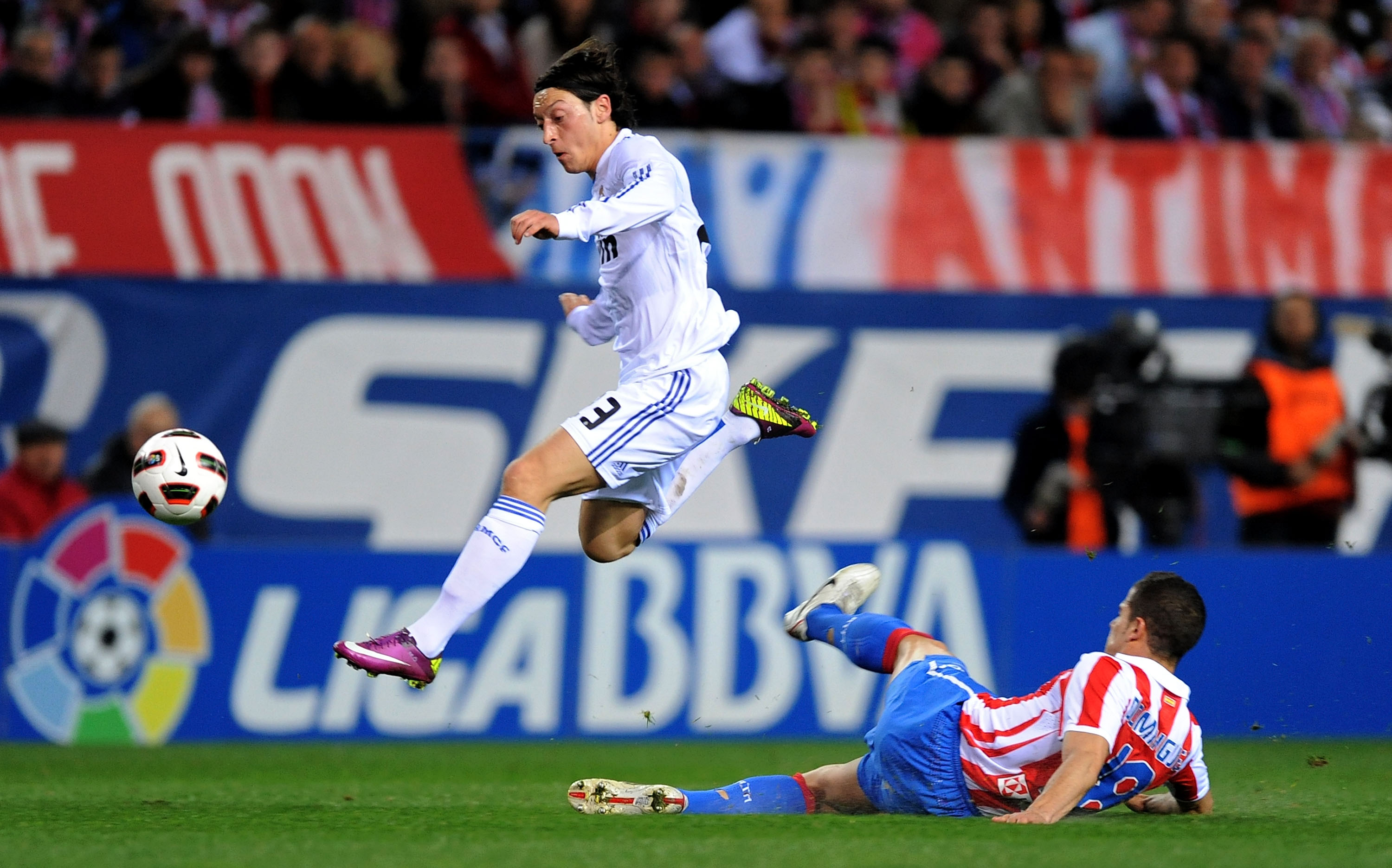 MADRID, SPAIN - MARCH 19:  Mesut Ozil (L) of Real Madrid avoids a late tackle by Alvaro Dominguez of Atletico Madrid during the La Liga match between Atletico Madrid and Real Madrid at Vicente Calderon Stadium on March 19, 2011 in Madrid, Spain.  (Photo b