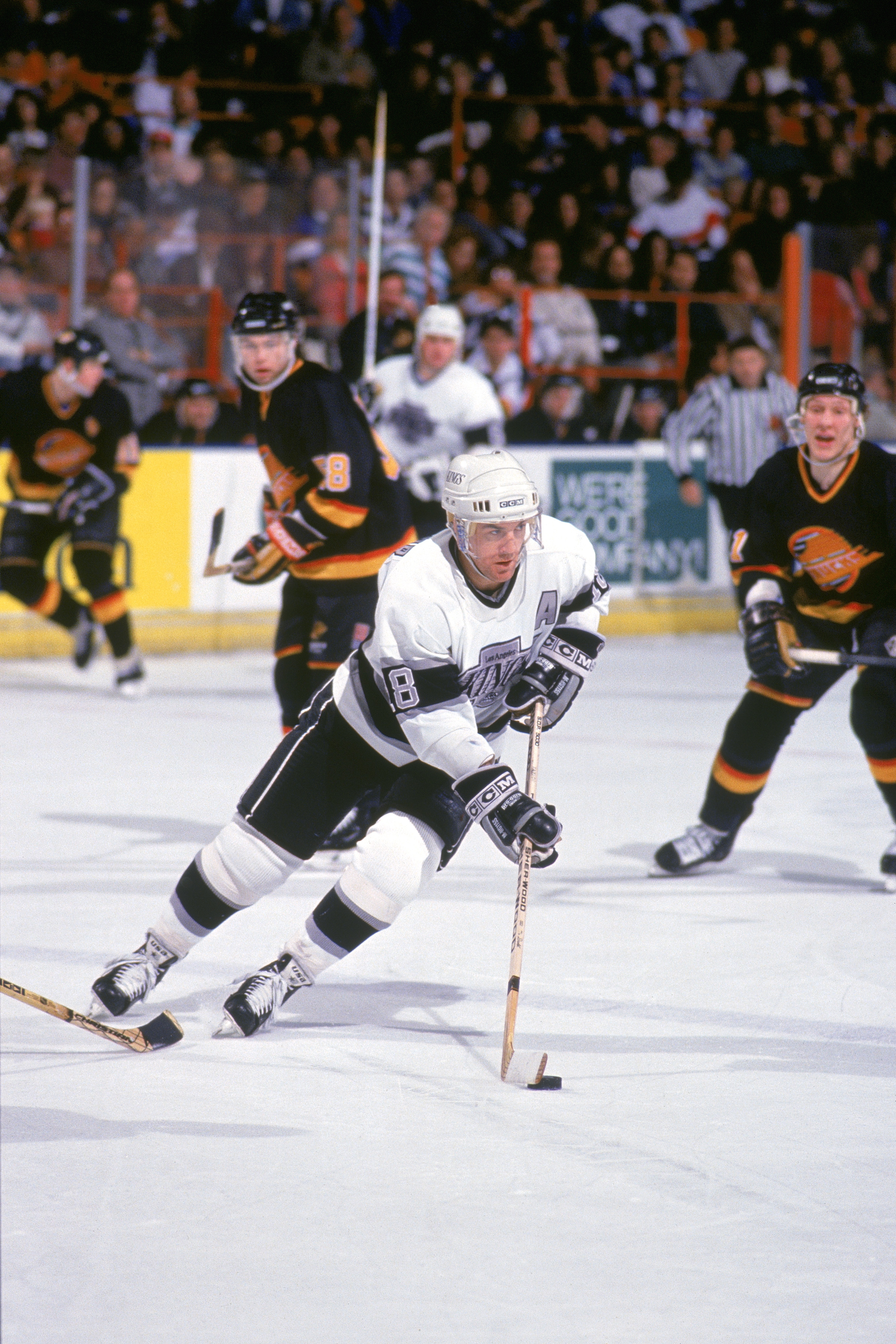 INGLEWOOD, CA - 1990:  Forward Dave Taylor #18 of the Los Angeles Kings skates with the puck against the Vancouver Canucks during the 1990-91 season at the Great Western Forum in Inglewood, California.  (Photo by Ken Levine/Getty Images)