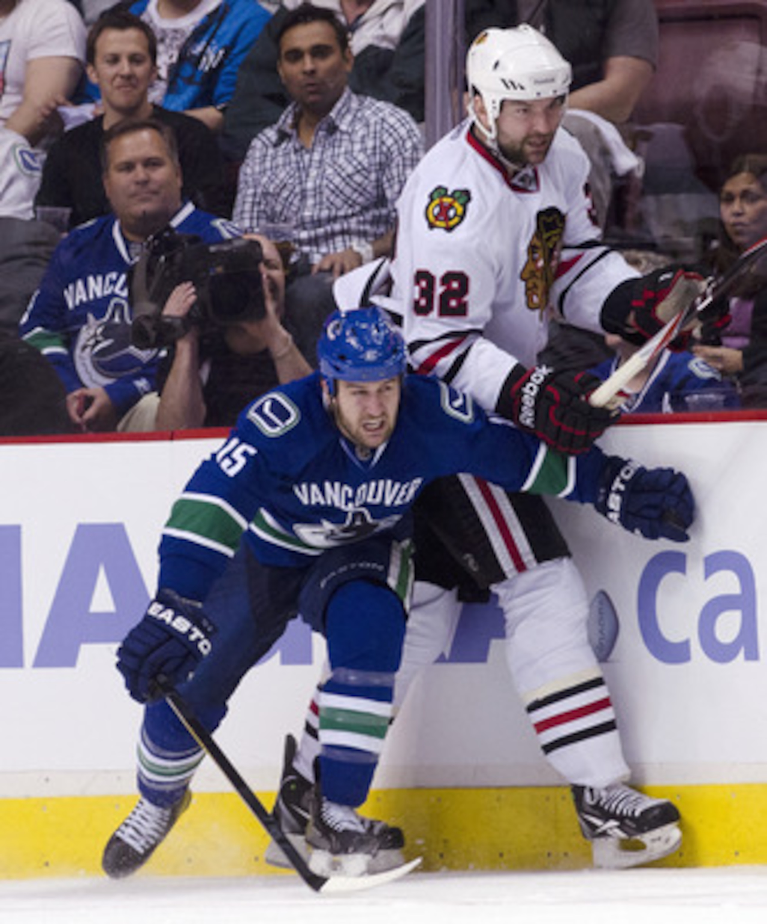 VANCOUVER, CANADA - APRIL 21: Tanner Glass #15 of the Vancouver Canucks hits John Scott #32 of the Chicago Blackhawks along the side boards during the third period in Game Five of the Western Conference Quarterfinals during the 2011 NHL Stanley Cup Playof