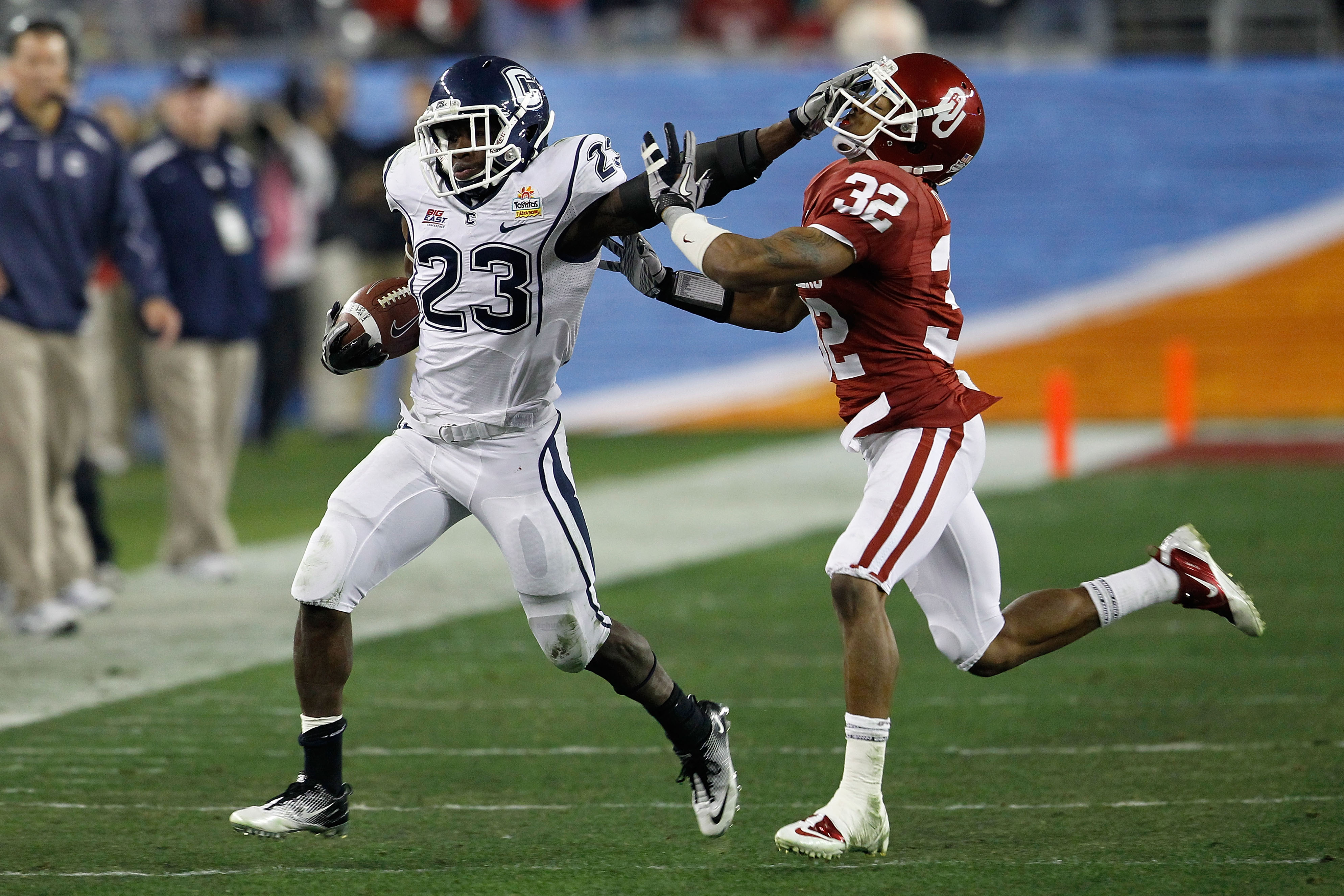GLENDALE, AZ - JANUARY 01:  Jordan Todman #23 of the Connecticut Huskies stiff arms Jamell Fleming #32 of the Oklahoma Sooners in the second quarter during the Tostitos Fiesta Bowl at the Universtity of Phoenix Stadium on January 1, 2011 in Glendale, Ariz