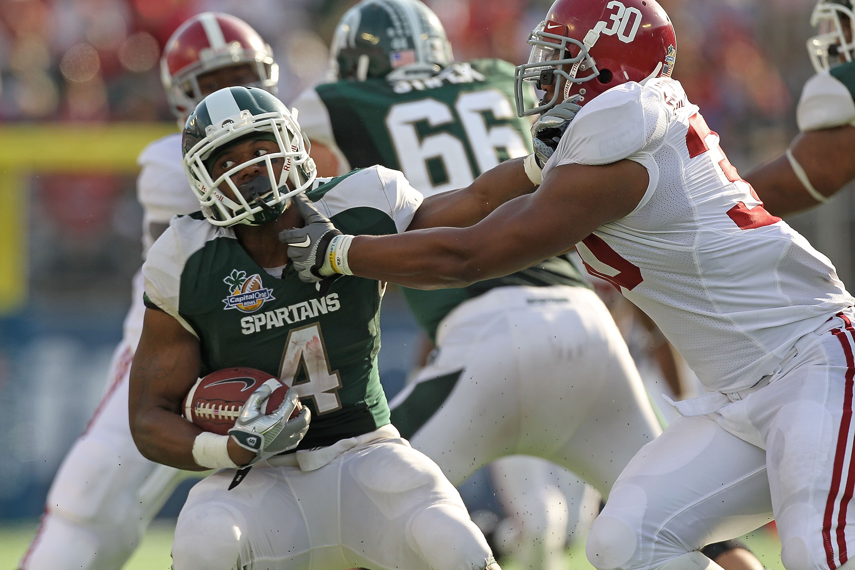 ORLANDO, FL - JANUARY 01:  Edwin Baker #4 of the Michigan State Spartans stiff arms Dont'a Hightower #30 of the Alabama Crimson Tide during the Capitol One Bowl at the Florida Citrus Bowl on January 1, 2011 in Orlando, Florida.  (Photo by Mike Ehrmann/Get