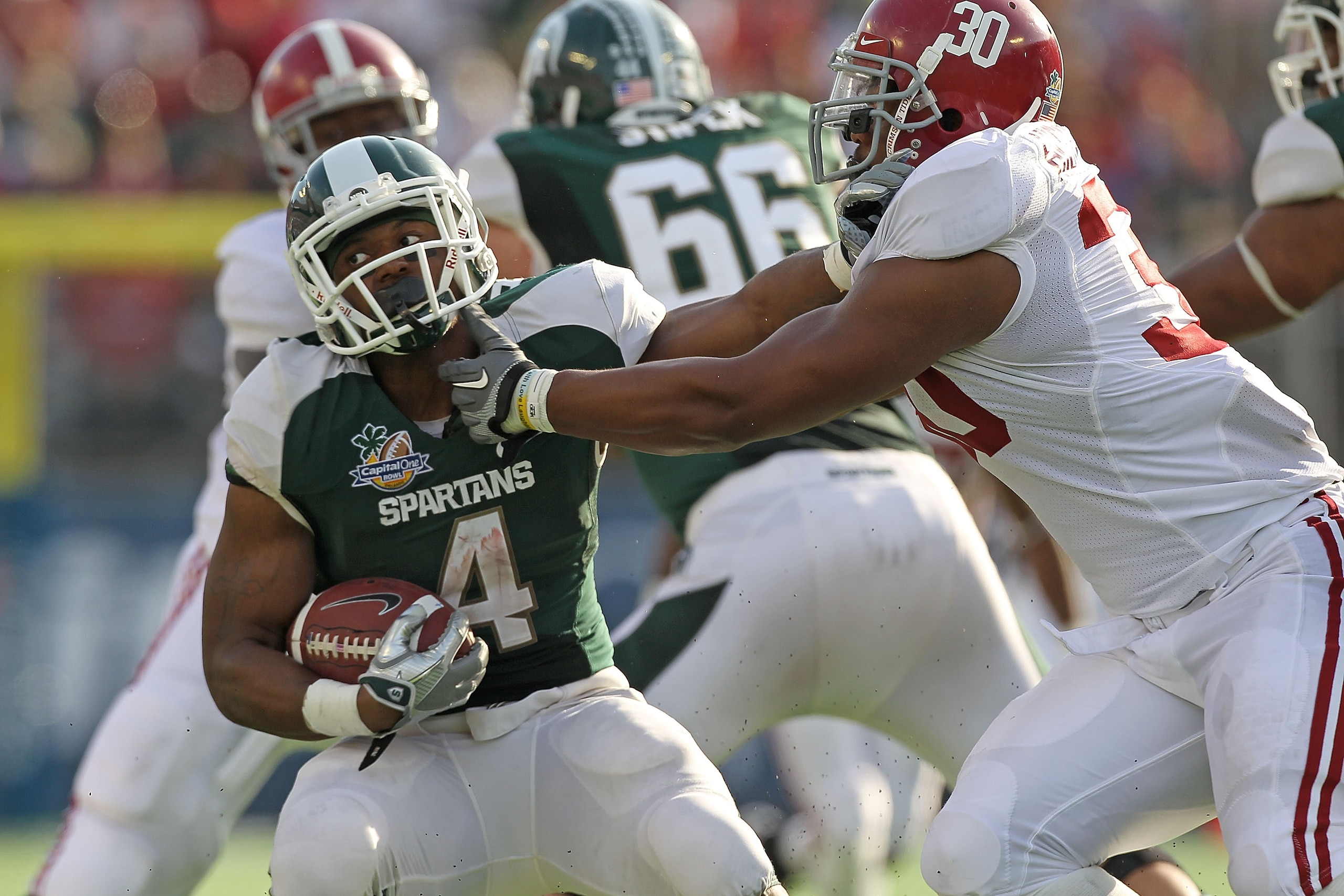 ORLANDO, FL - JANUARY 01:  Edwin Baker #4 of the Michigan State Spartans stiff arms Dont'a Hightower #30 of the Alabama Crimson Tide during the Capitol One Bowl at the Florida Citrus Bowl on January 1, 2011 in Orlando, Florida.  (Photo by Mike Ehrmann/Get