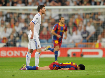 MADRID, SPAIN - APRIL 27:  Xabi Alonso (L) of Real Madrid stands besides Pedro Rodriguez of Barcelona laying on the pitch during the UEFA Champions League Semi Final first leg match between Real Madrid and Barcelona at the Estadio Santiago Bernabeu on Apr