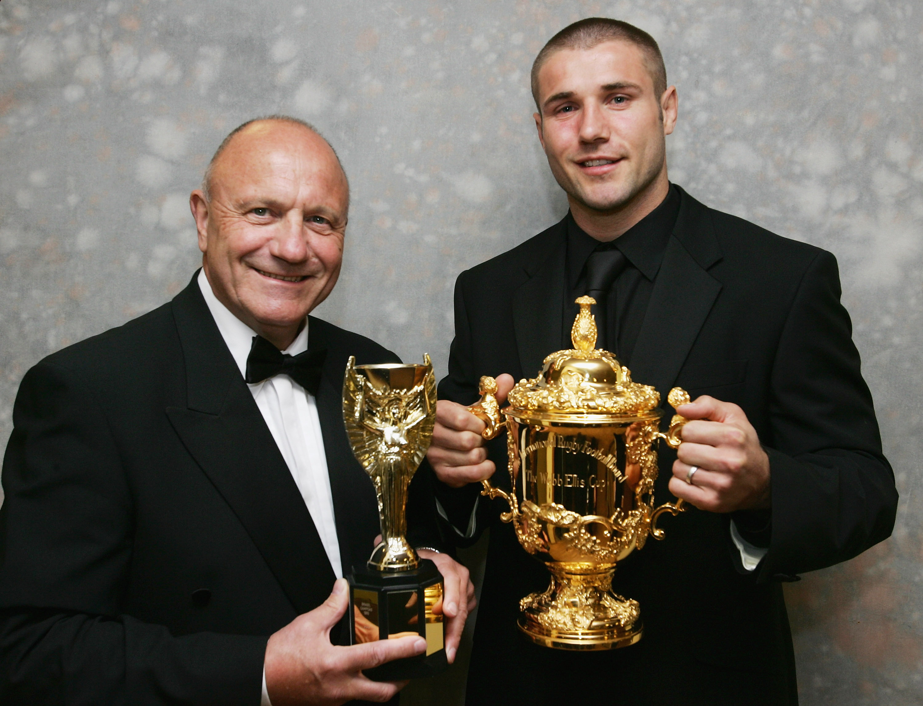 NORTHAMPTON, UNITED KINGDOM - MAY 3:   George Cohen (L) poses with a replica of the Jules Rimet Trophy (which he won in 1966 as part of the England World Cup winning footbal team) and his nephew Ben Cohen, holding the Webb Ellis Trophy (which he won as pa