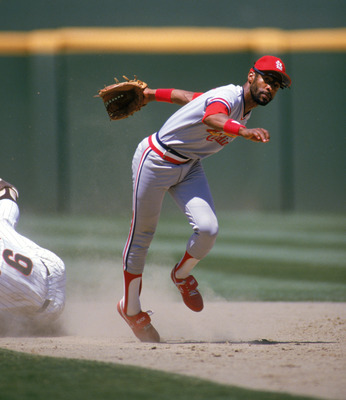 SAN DIEGO - 1985:  Ozzie Smith #1 of the St. Louis Cardinals stumbles after dodging a sliding San Diego Padres base runner during a game in 1985 at Jack Murphy Stadium in San Diego, California.  (Photo by Stephen Dunn/Getty Images)