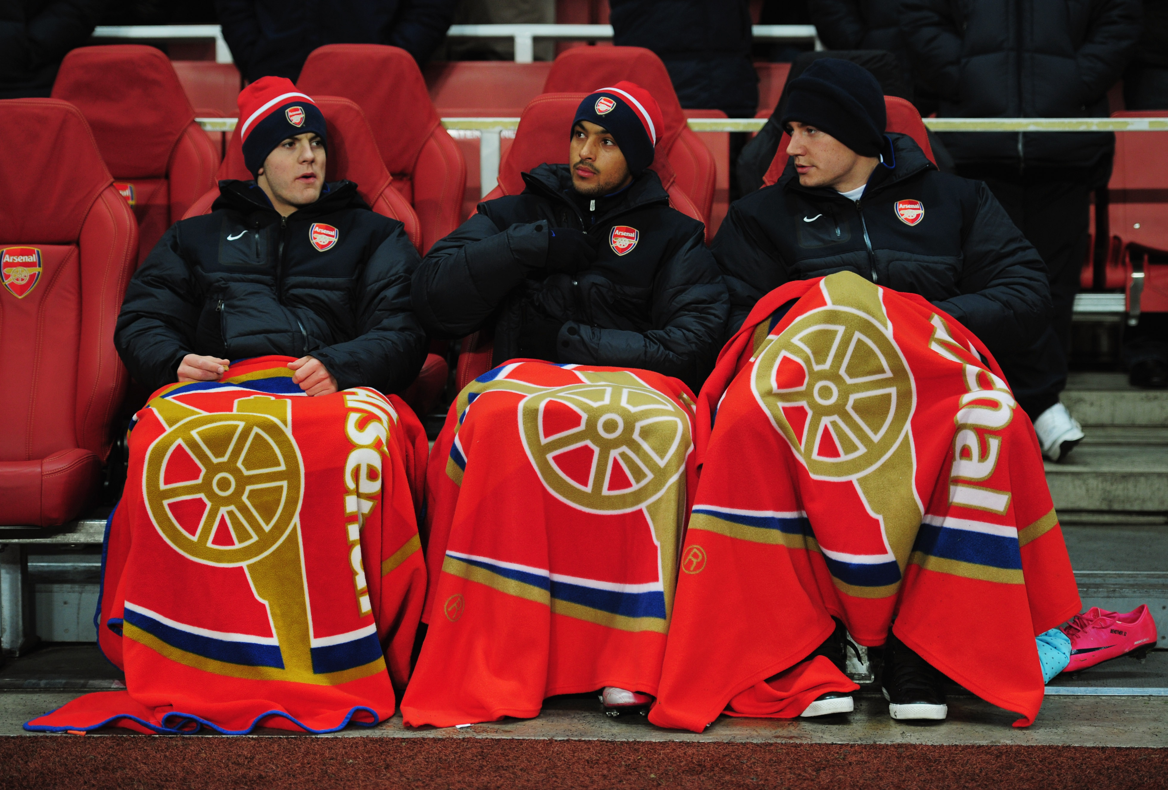 LONDON, ENGLAND - DECEMBER 08:  Substitutes Jack Wilshere, Theo Walcott and Nicklas Bendtner of Arsenal attempt to keep warm as they sit on the bench prior to the UEFA Champions League Group H match between Arsenal and FK Partizan Belgrade at the Emirates